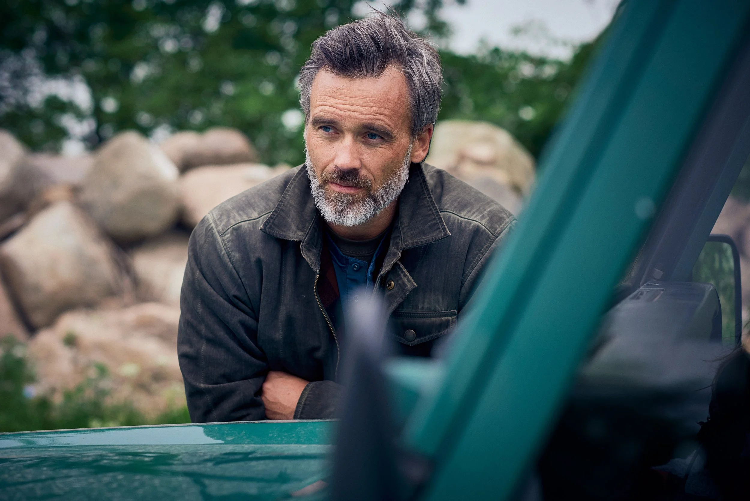Man leaning on vehicle in rural setting, reflective moment before or after hunt
