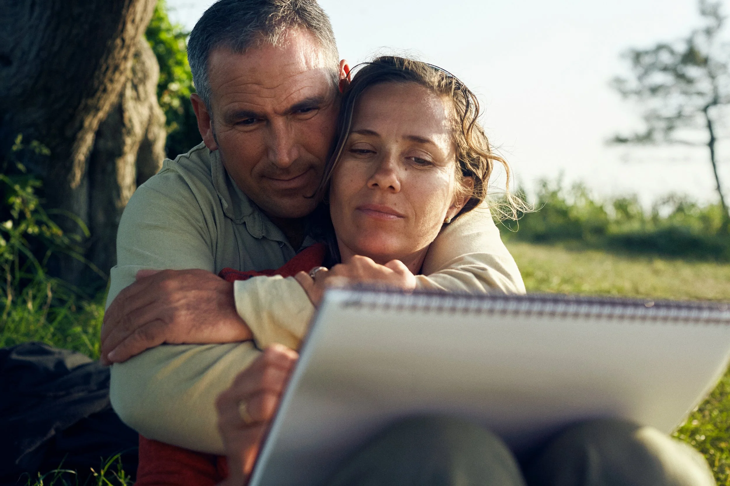 Couple sitting outdoors looking at sketchbook, quiet moment in nature