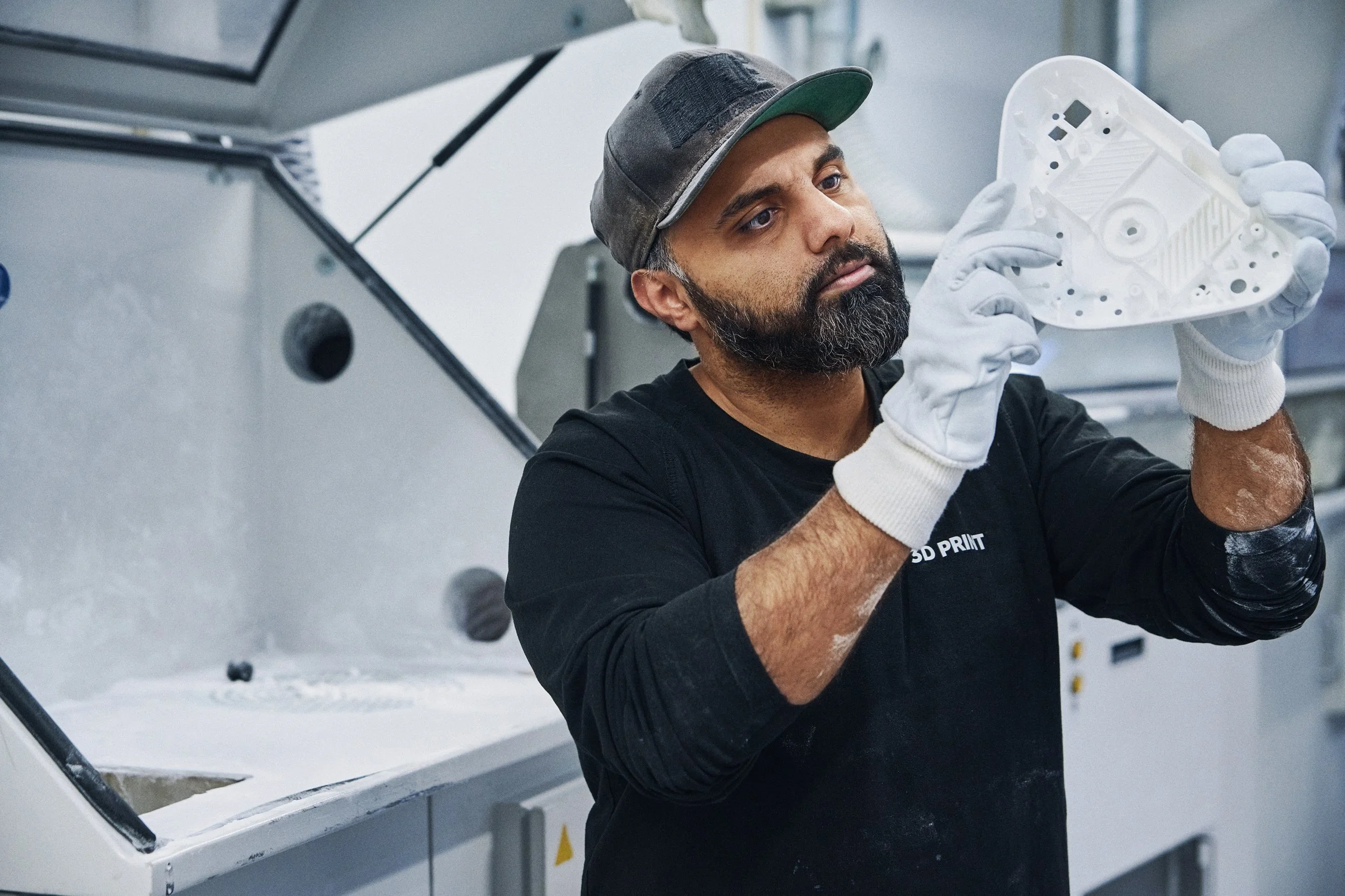 Technician inspecting white 3D printed component in workshop, quality control task