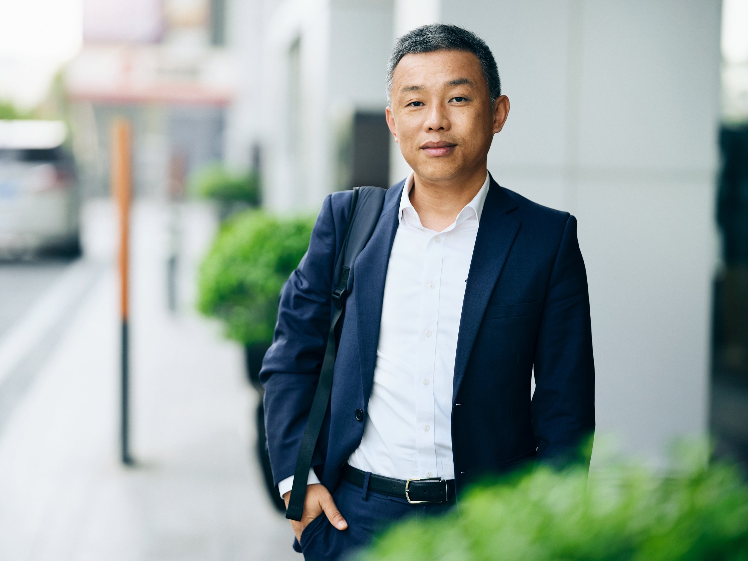 Business professional standing outdoors in city environment, wearing suit and carrying shoulder bag, natural portrait