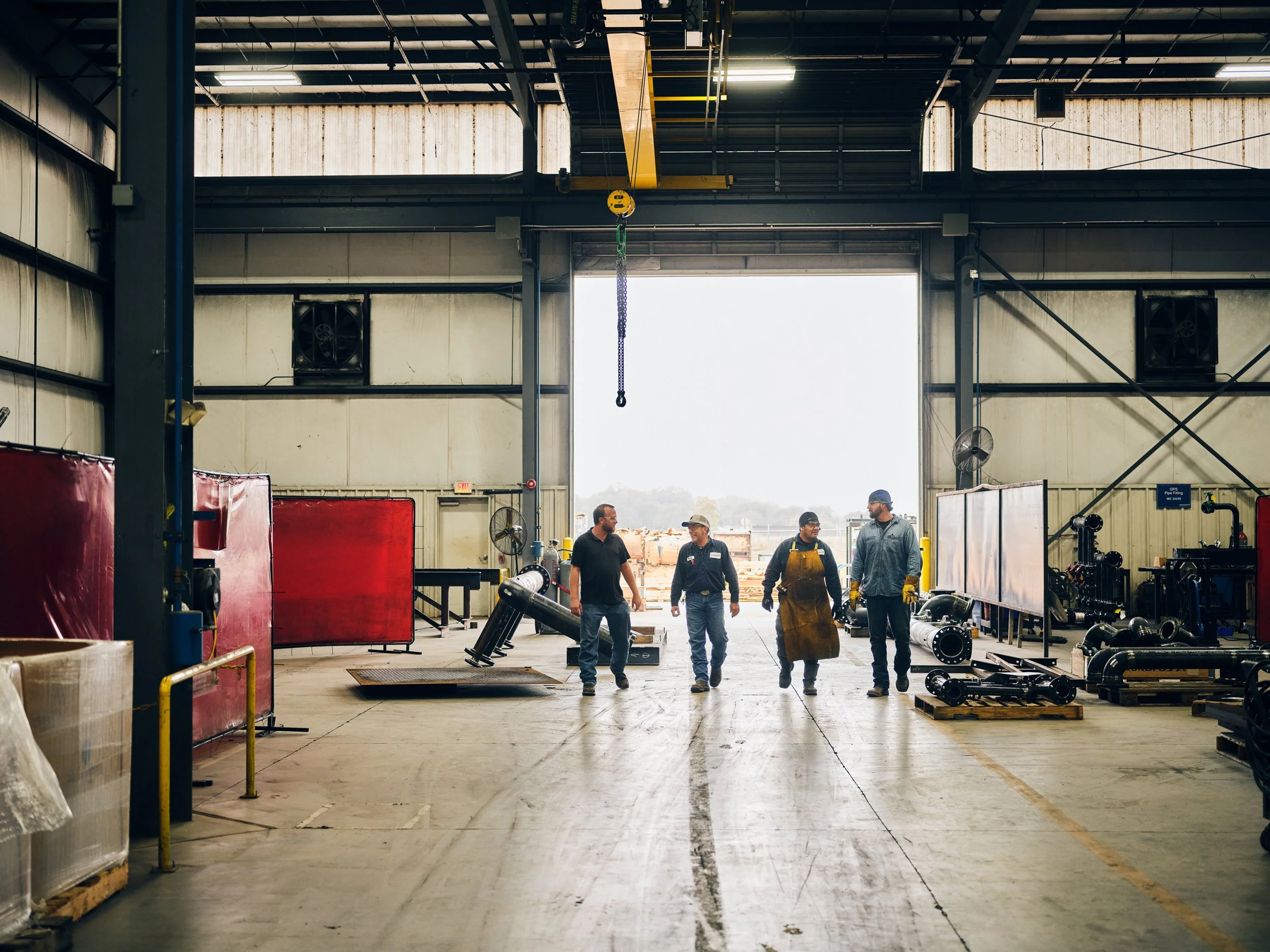 Group of factory workers walking through large industrial hall with equipment and machinery