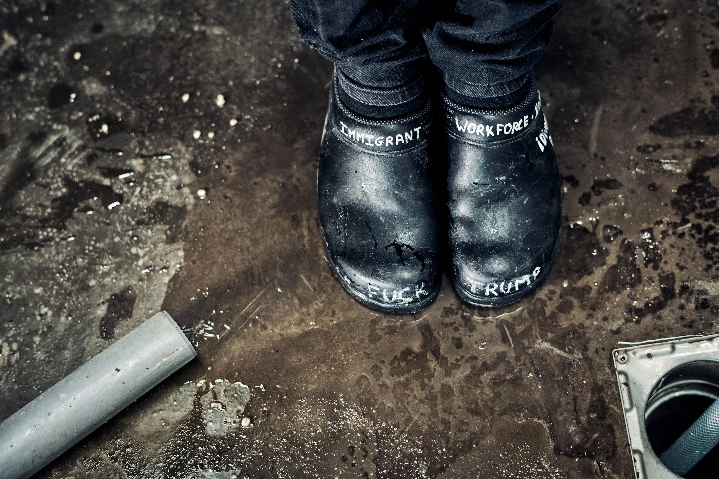 Rubber boots on wet floor in distillery, raw working conditions and material detail, provocative text on the boots.