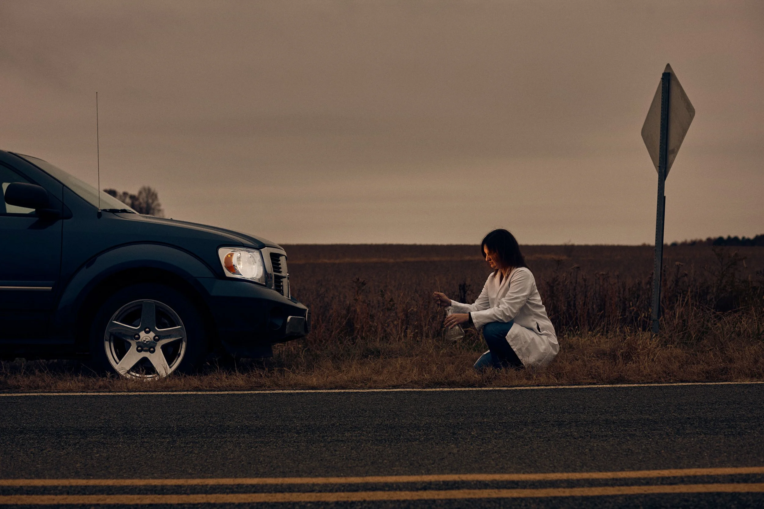 Field technician collecting roadside sample near vehicle, applied science in real-world conditions
