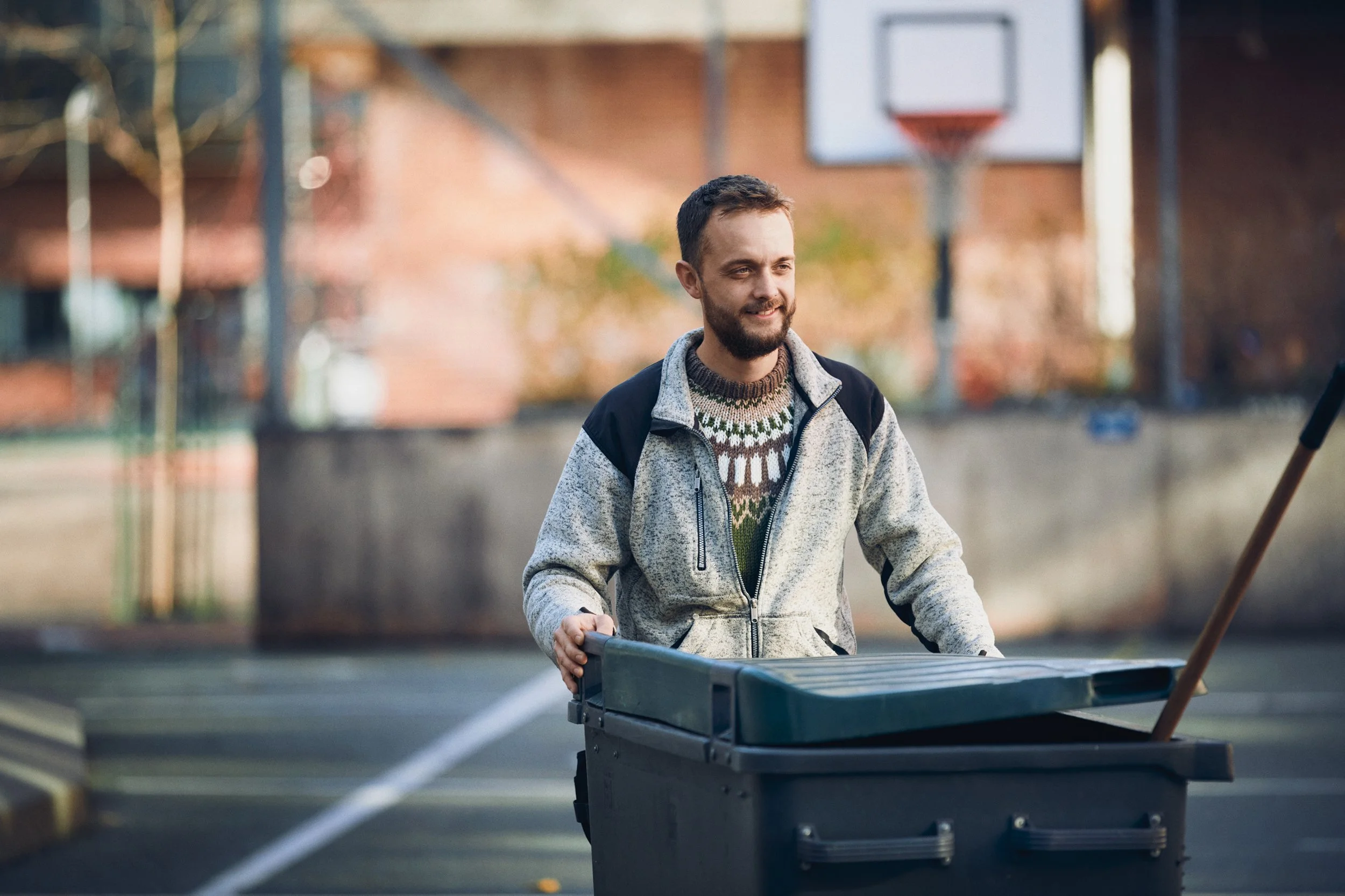Man pushing large bin in outdoor courtyard, everyday work task