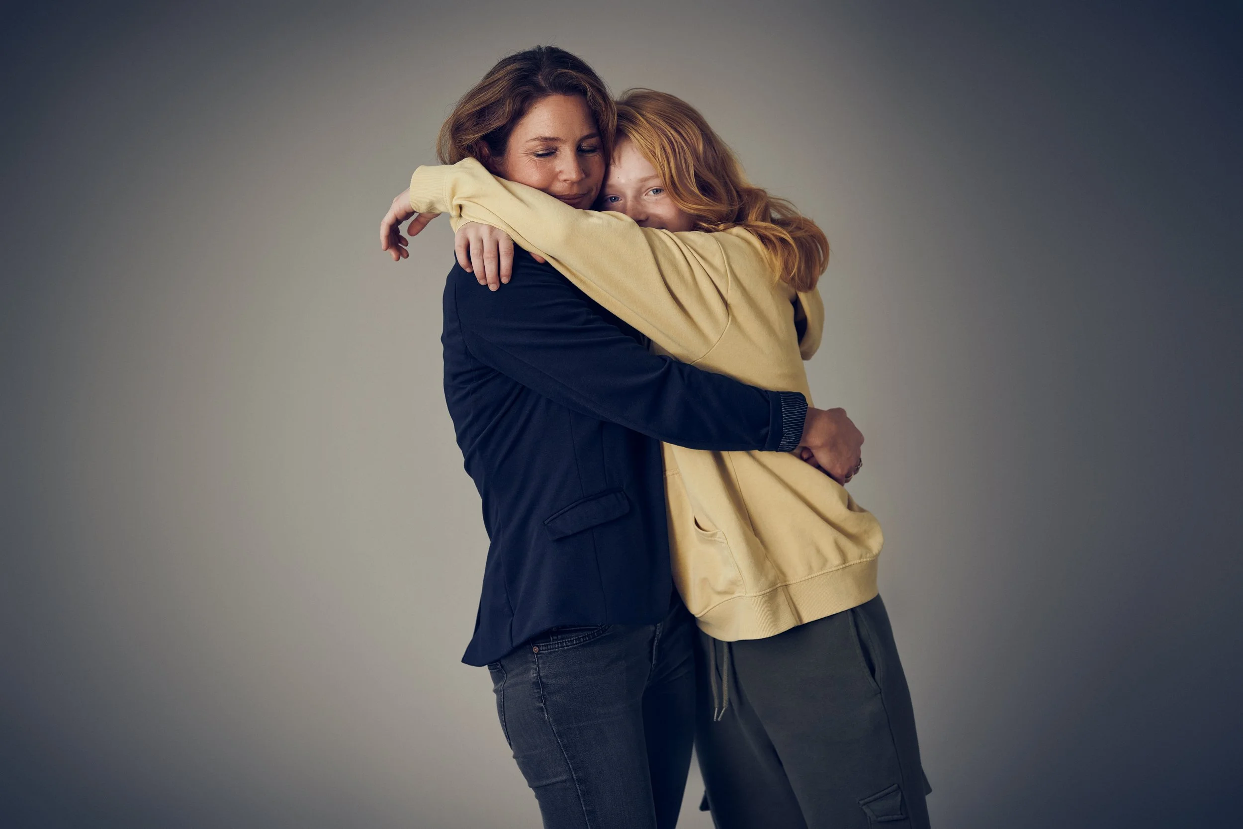 Two women embracing each other, intimate moment against neutral background