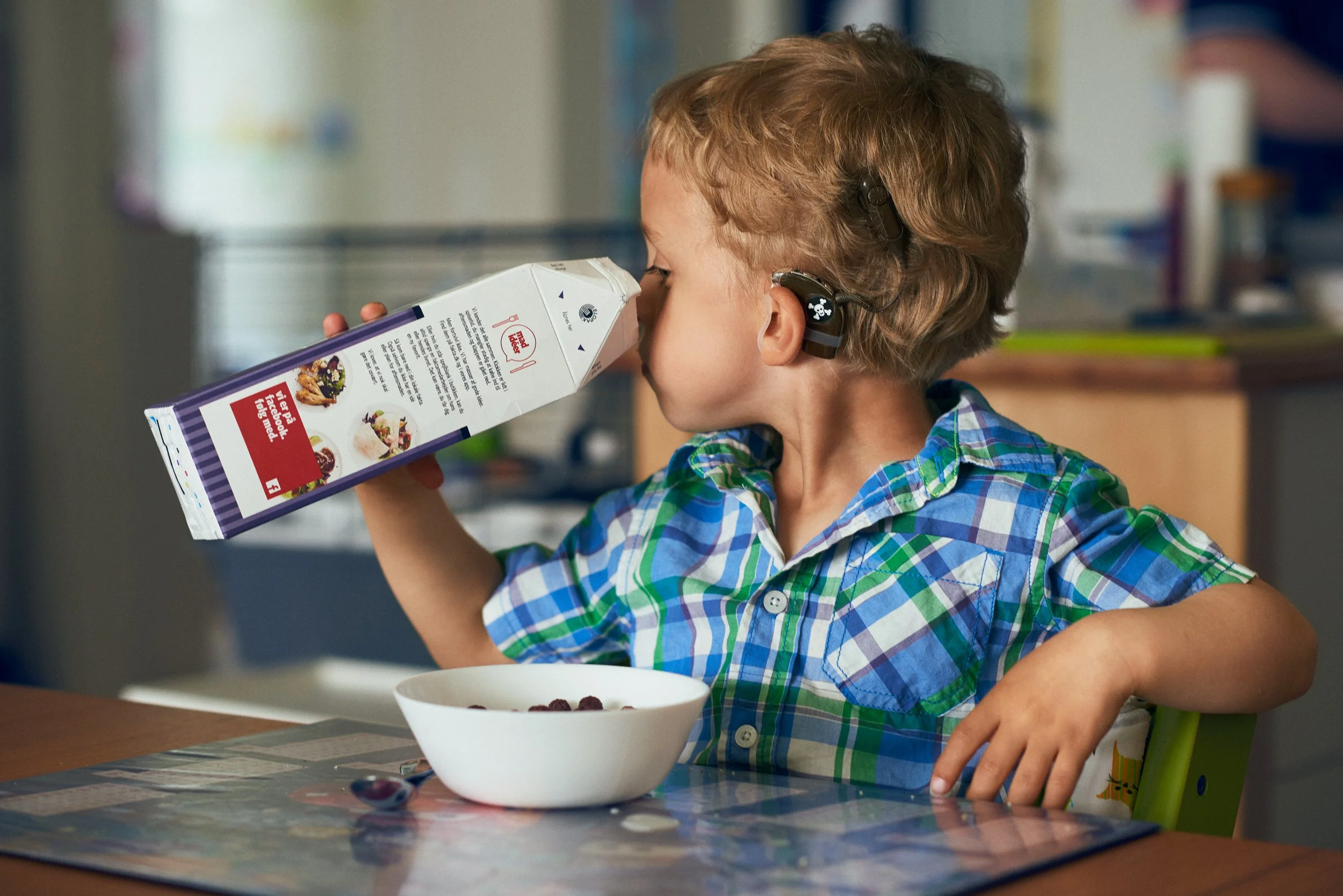 Child with cochlear implants looking in a milk carton at table, everyday routine
