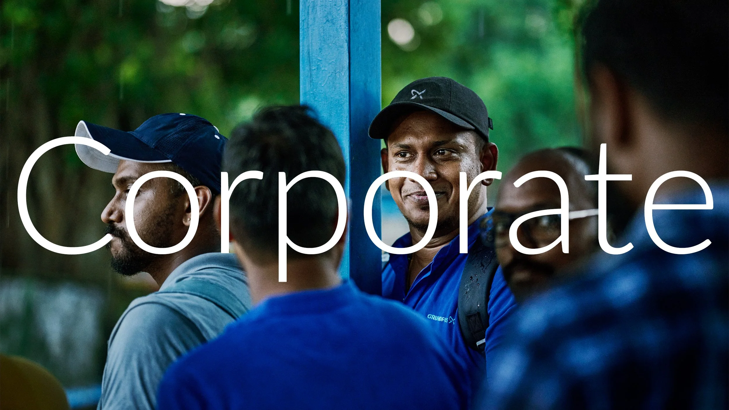 A group of men, some wearing caps, sitting closely together outdoors with a green, leafy background. The word 'capture' is overlaid on the image.