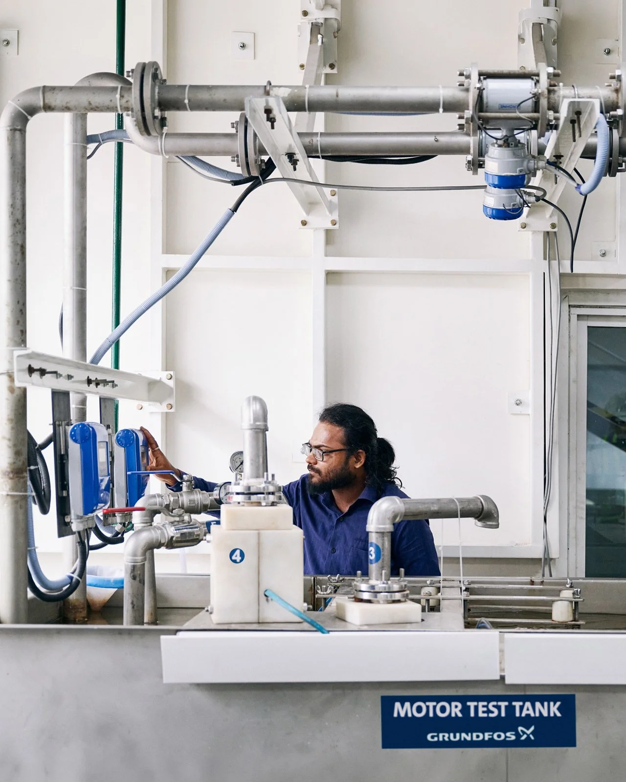 A man working with pipes and machinery in a laboratory setting, labeled 'Motor Test Tank'.