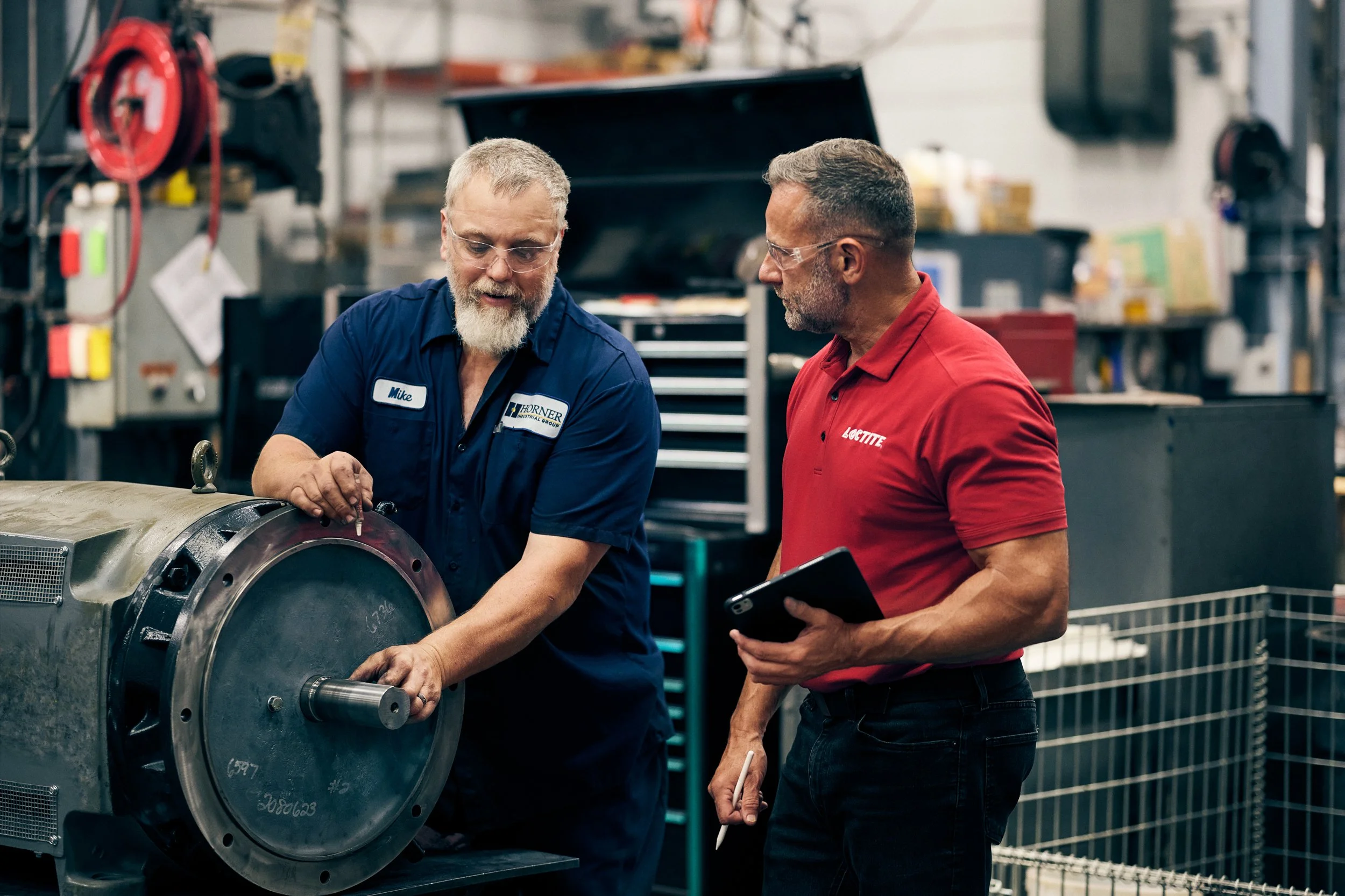 Worker and technician inspecting industrial motor component in workshop