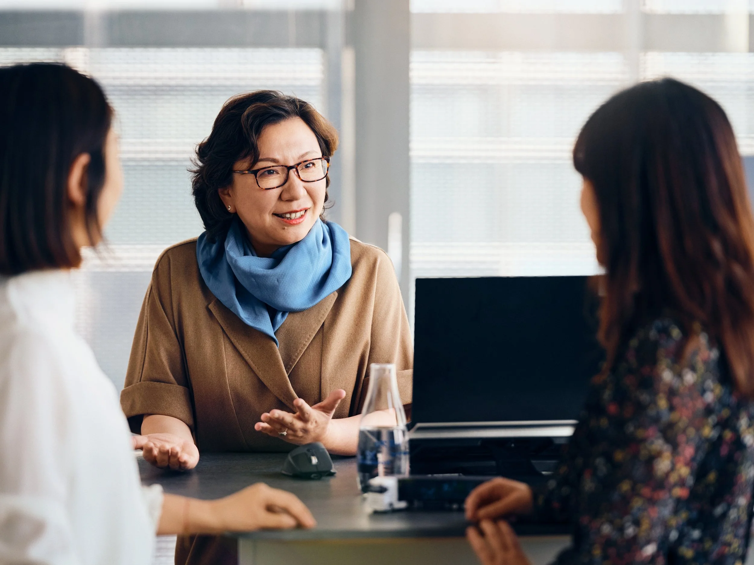 Professional Business Woman leading meeting with two colleagues in office setting, discussion around laptop and table