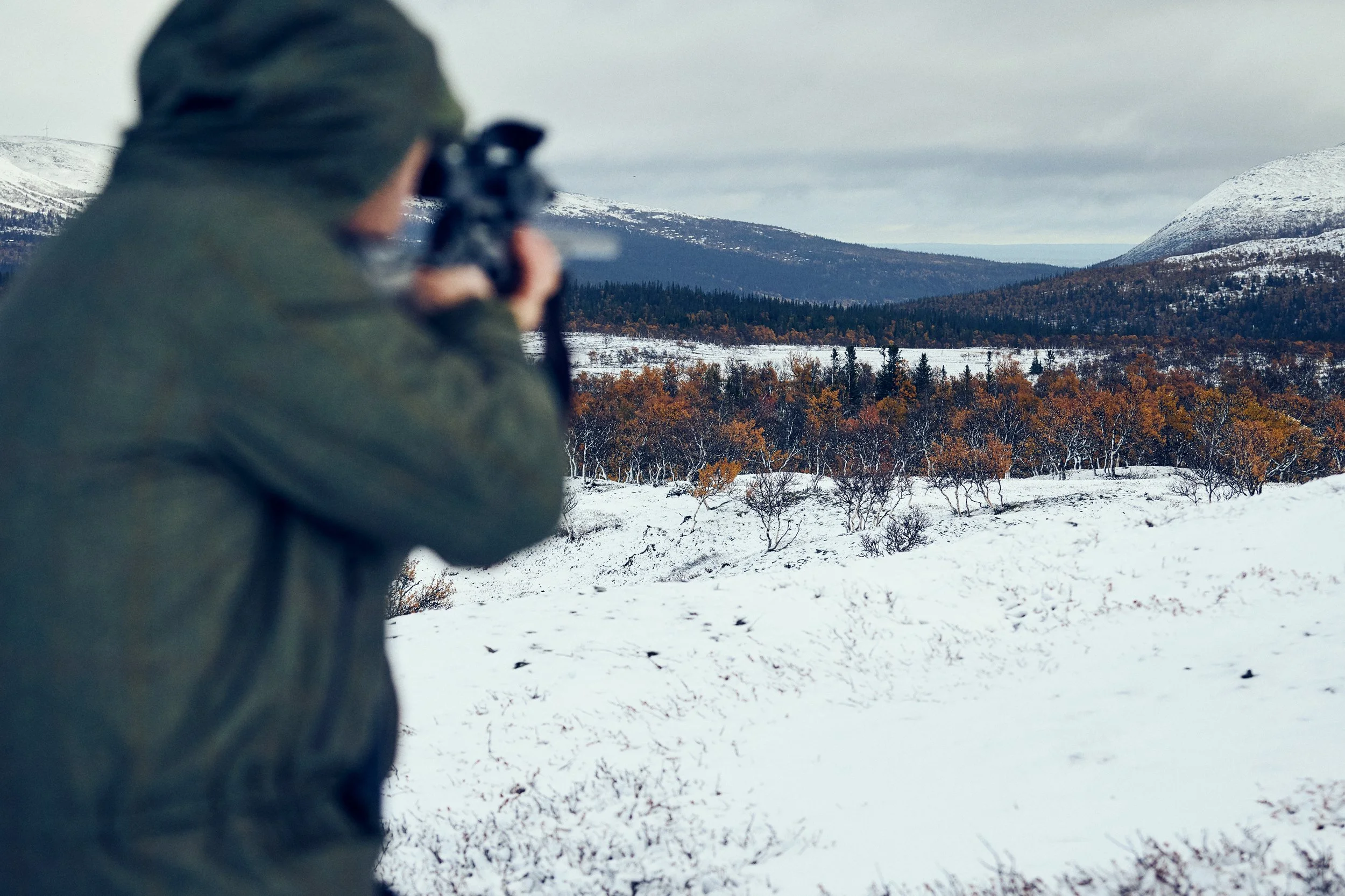 Hunter aiming rifle across snowy landscape, focus on distant target