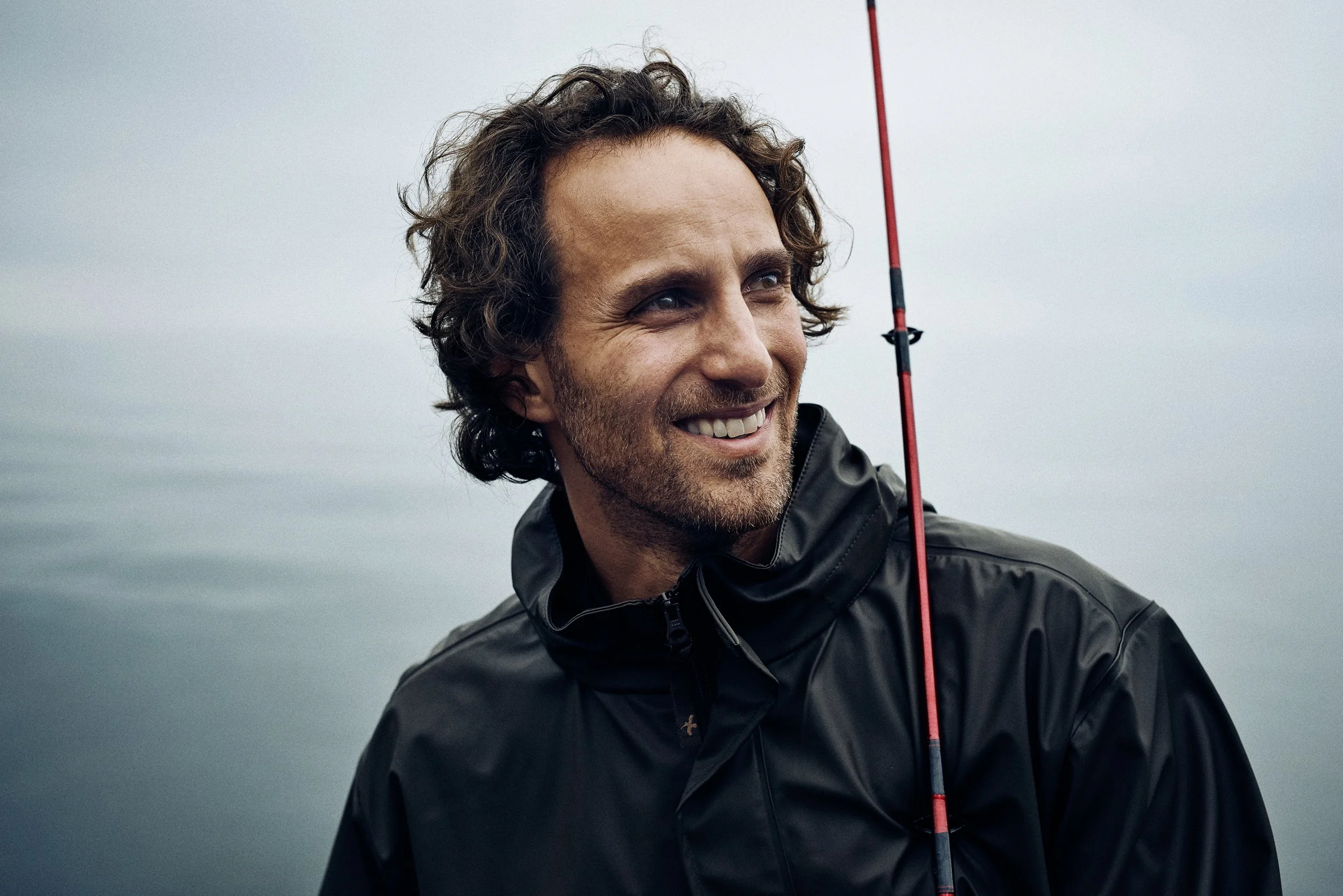 Portrait of man holding fishing rod, relaxed expression by the sea