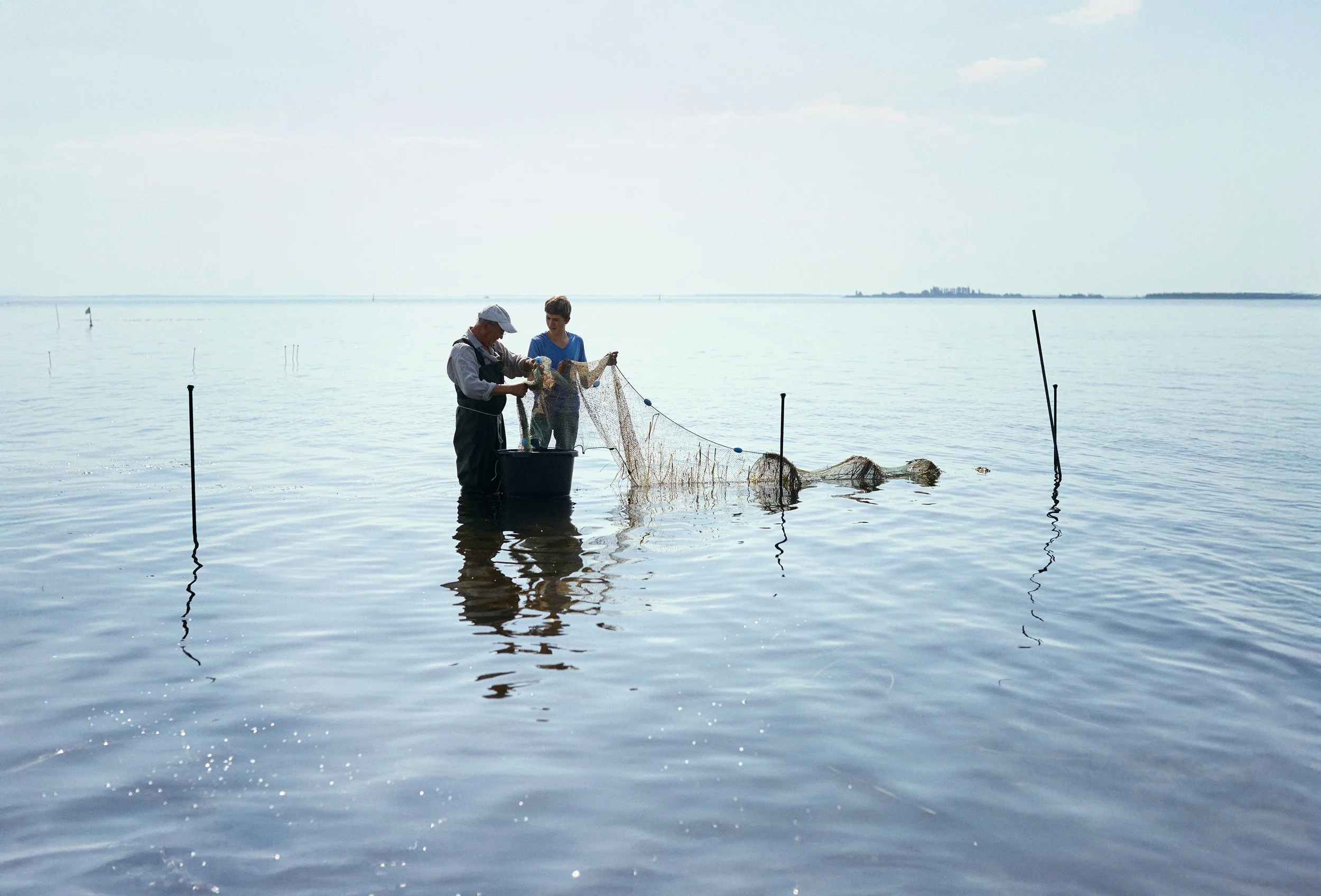 Two people standing in shallow water handling fishing net, coastal activity