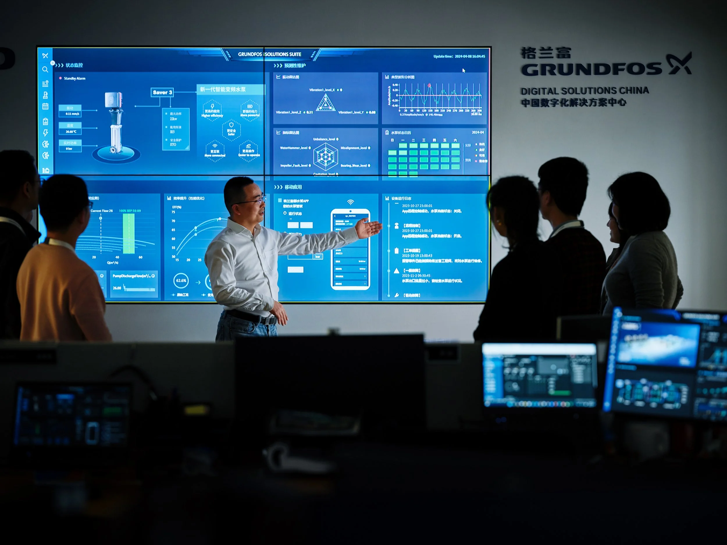 Engineer presenting real-time system data on large digital interface to team in control room