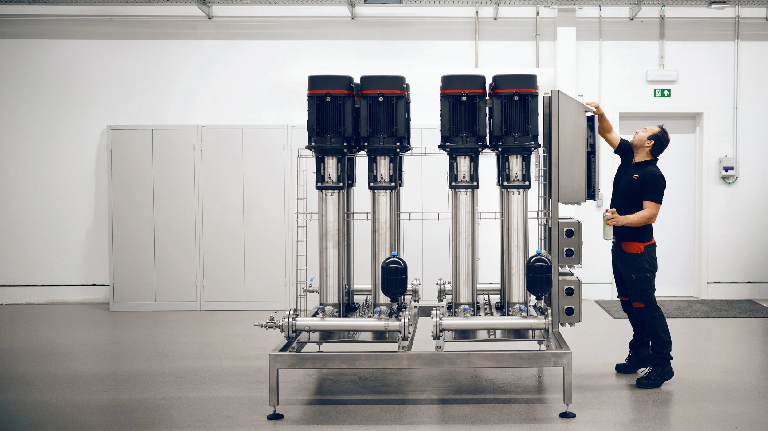 A man inspecting an industrial water filtration system in a clean, white room.