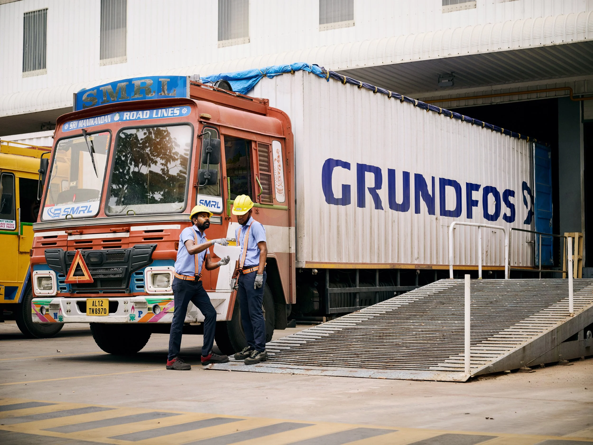 Truck parked outside Grundfos facility with workers in conversation near loading area