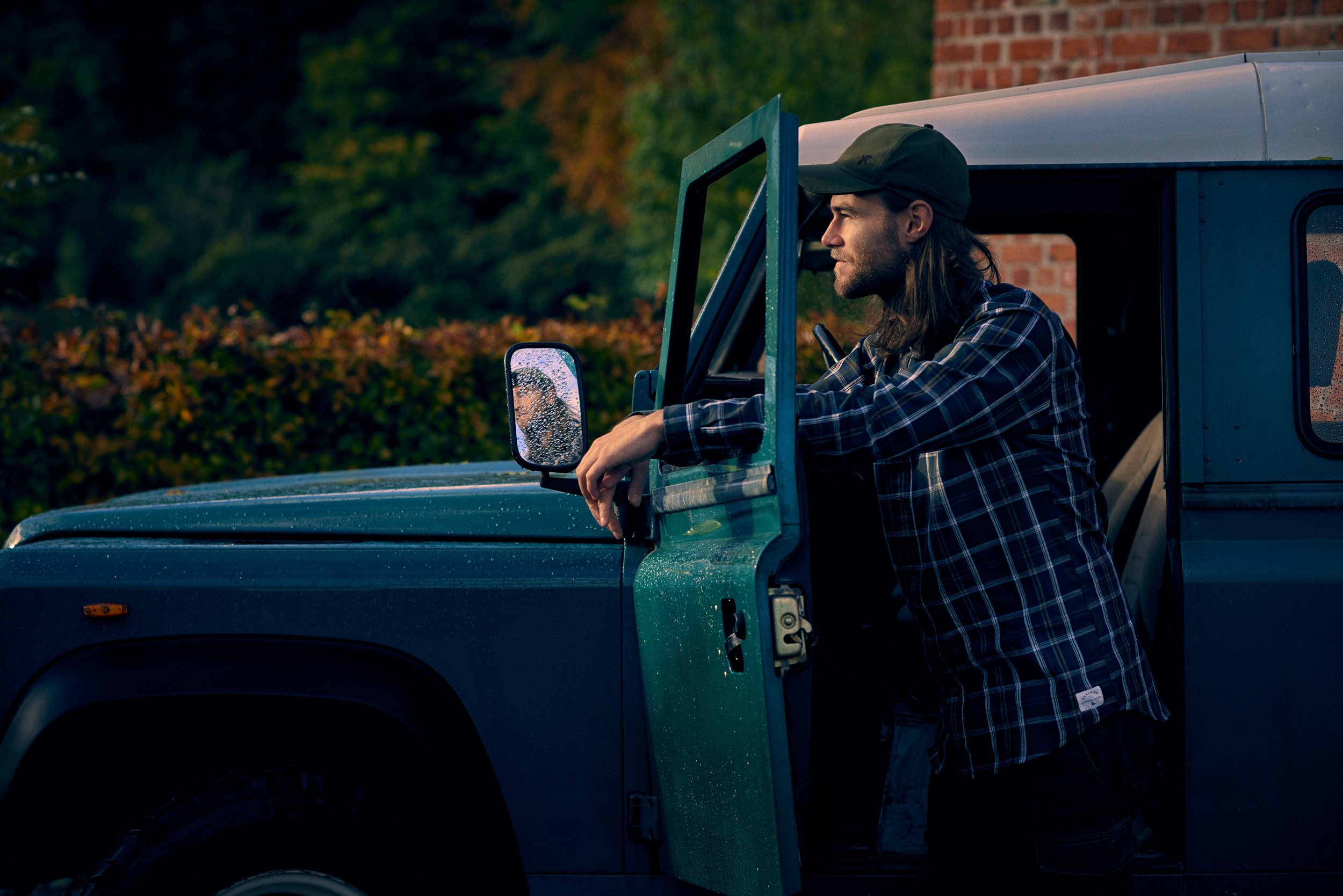 Man leaning on open vehicle door, paused moment before or after field activity