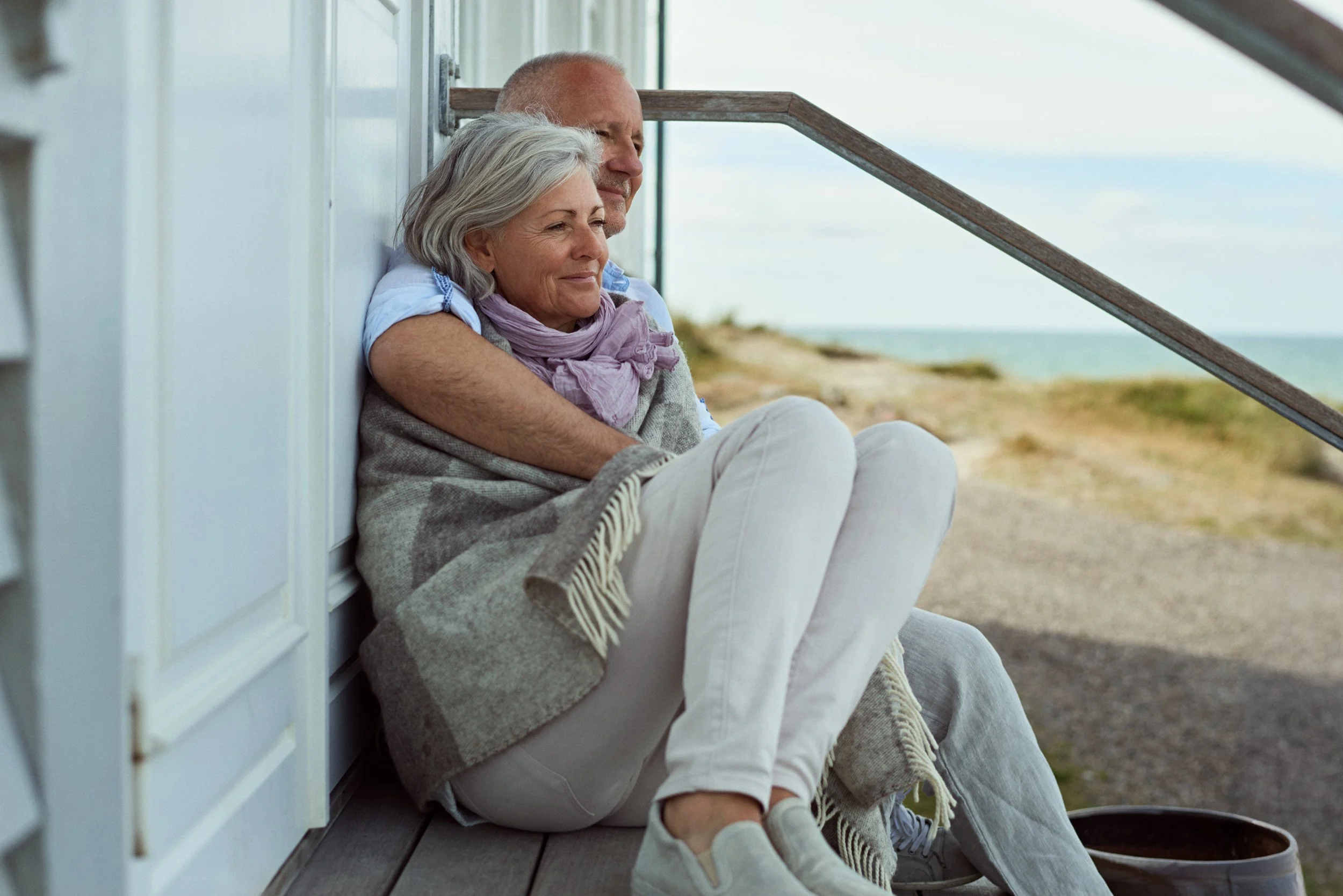 Older couple sitting together by seaside house, quiet shared moment