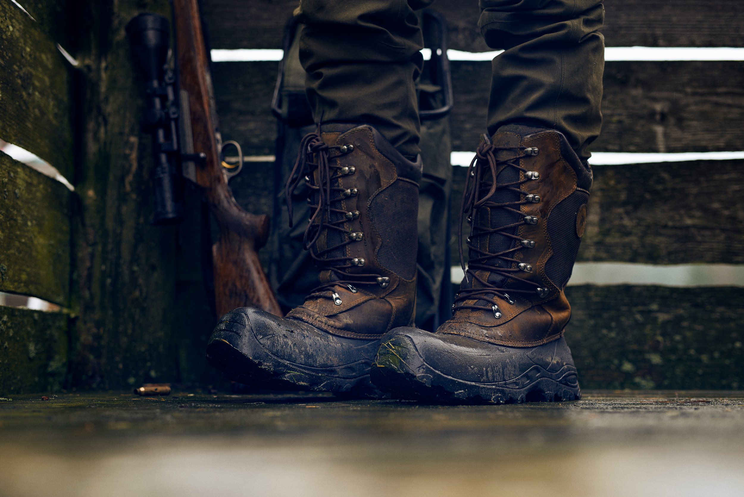 Close-up of muddy hunting boots on wooden surface, gear detail after field use