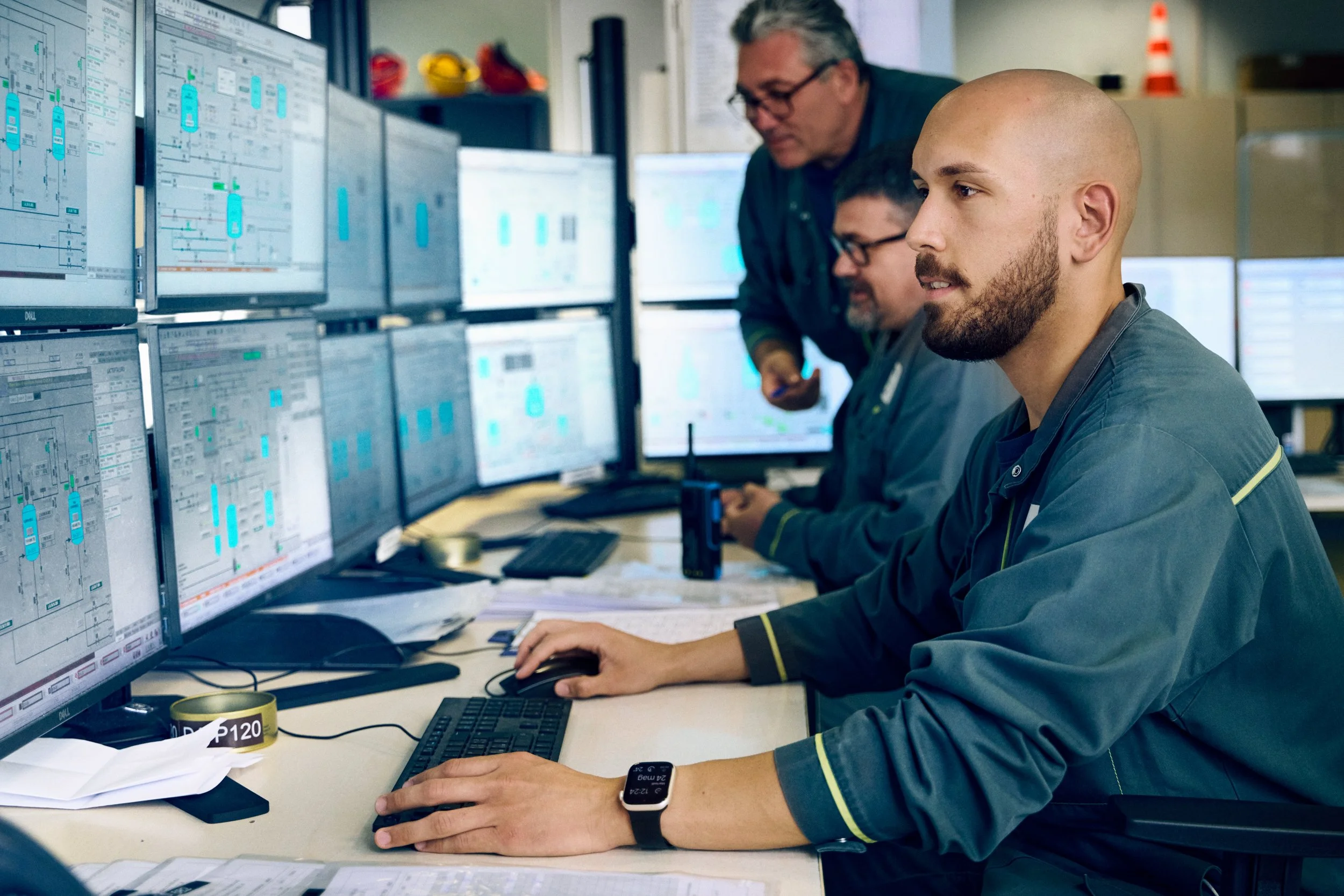 Operators monitoring production systems on multiple screens in control room