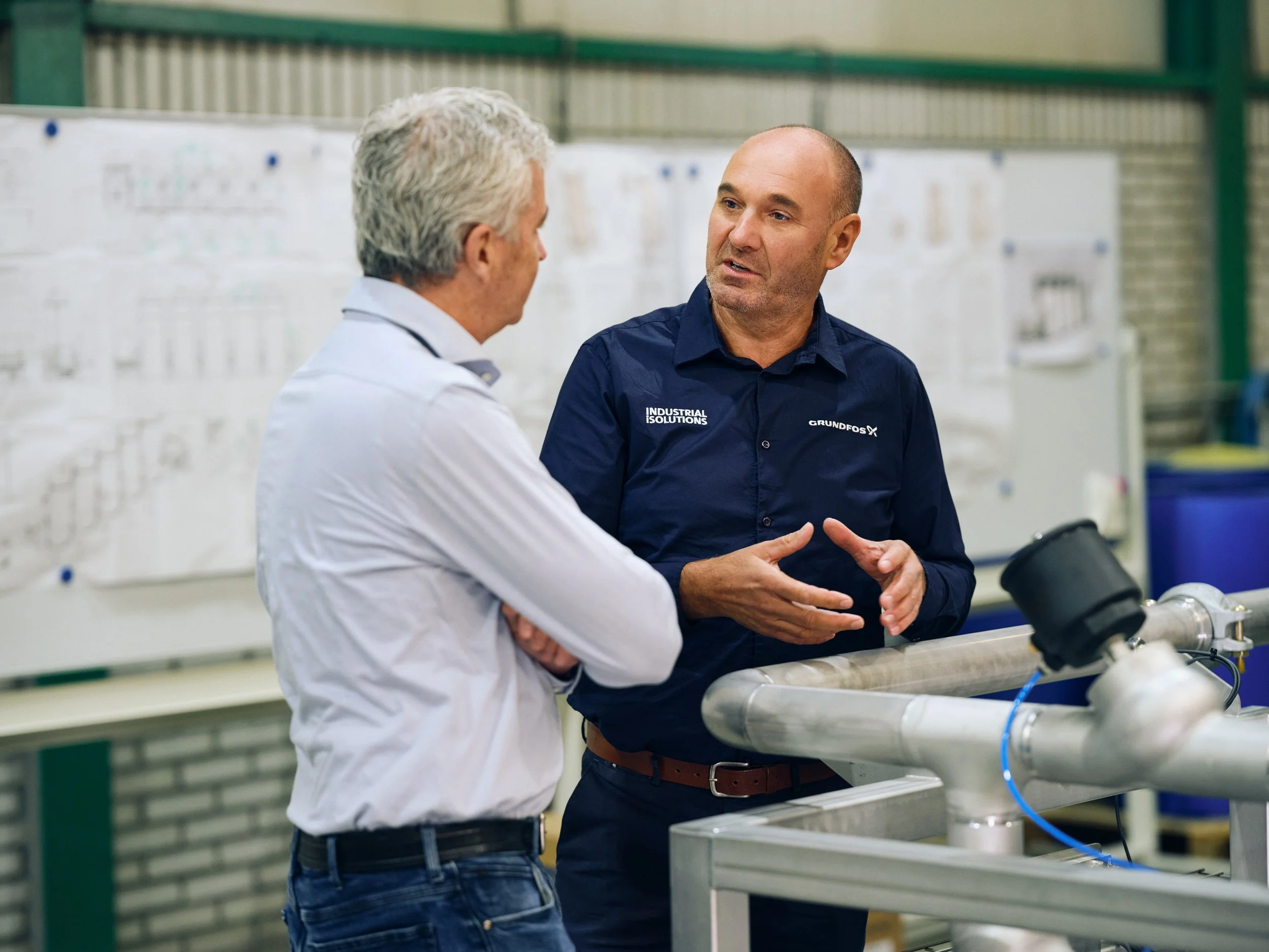 Two men discussing technical system next to pipes and equipment
