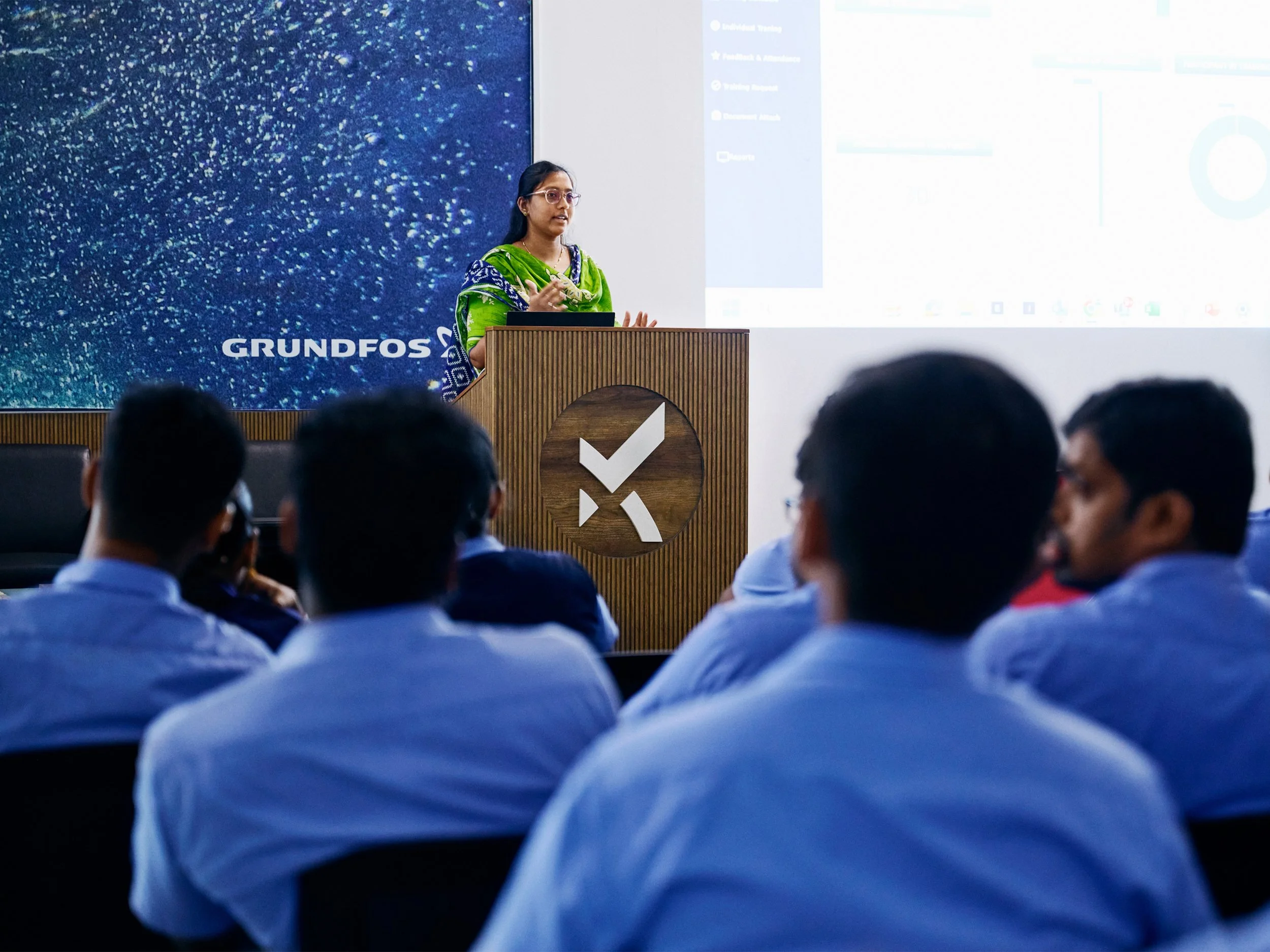 Female speaker presenting at corporate event with audience seated in conference room
