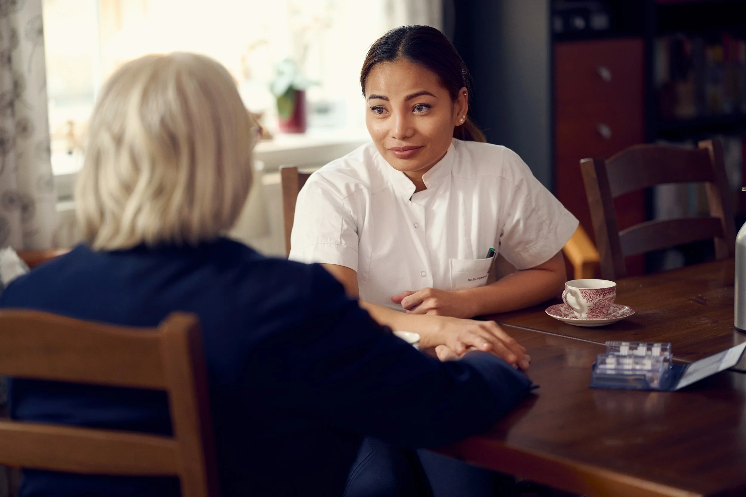 Healthcare worker speaking with older person at table, supportive interaction indoors