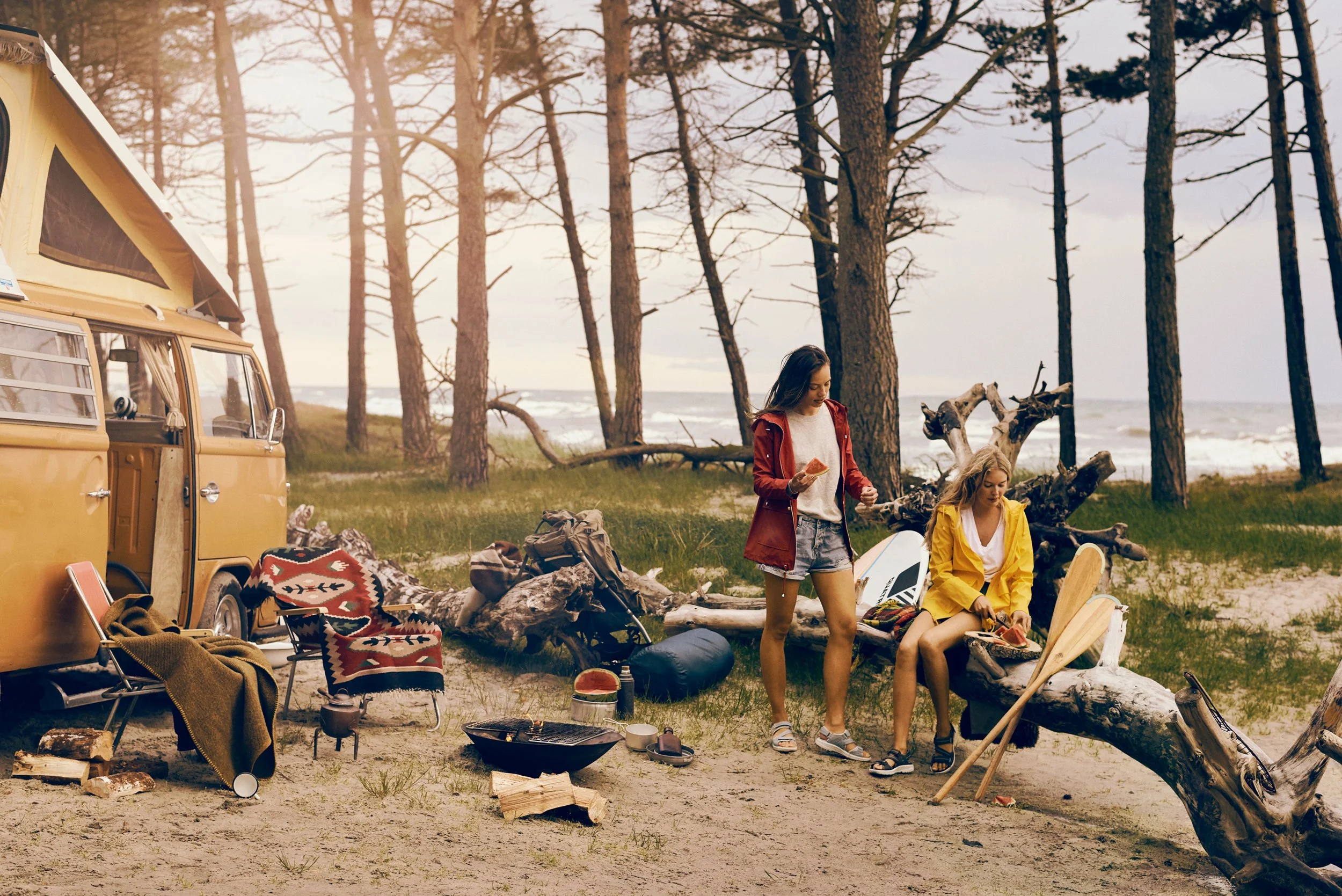 Two women at campsite by beach with van and outdoor gear