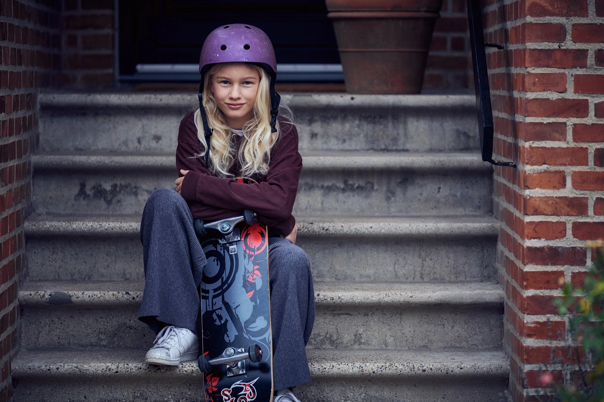 Girl sitting on stairs with skateboard, casual moment in residential setting