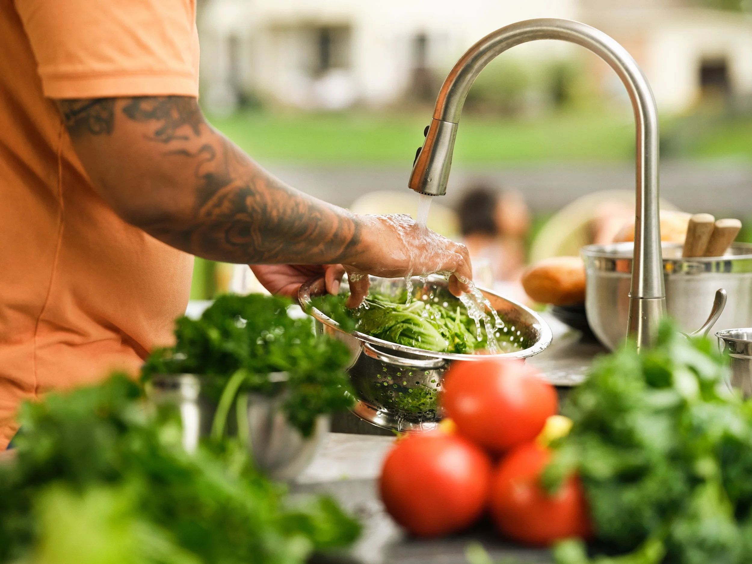 Person washing vegetables under kitchen faucet with running water