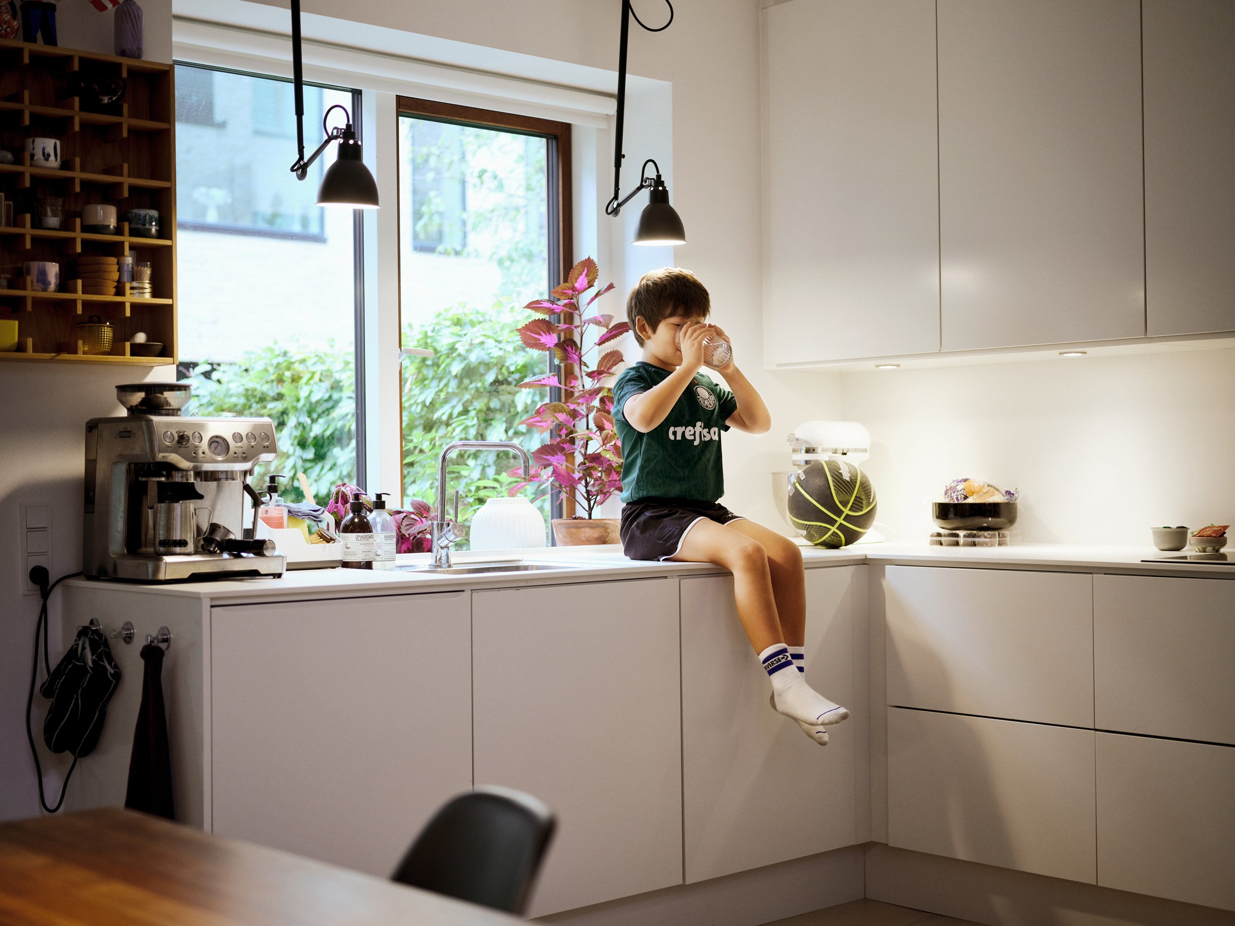 Child sitting on kitchen counter drinking from glass in modern home interior