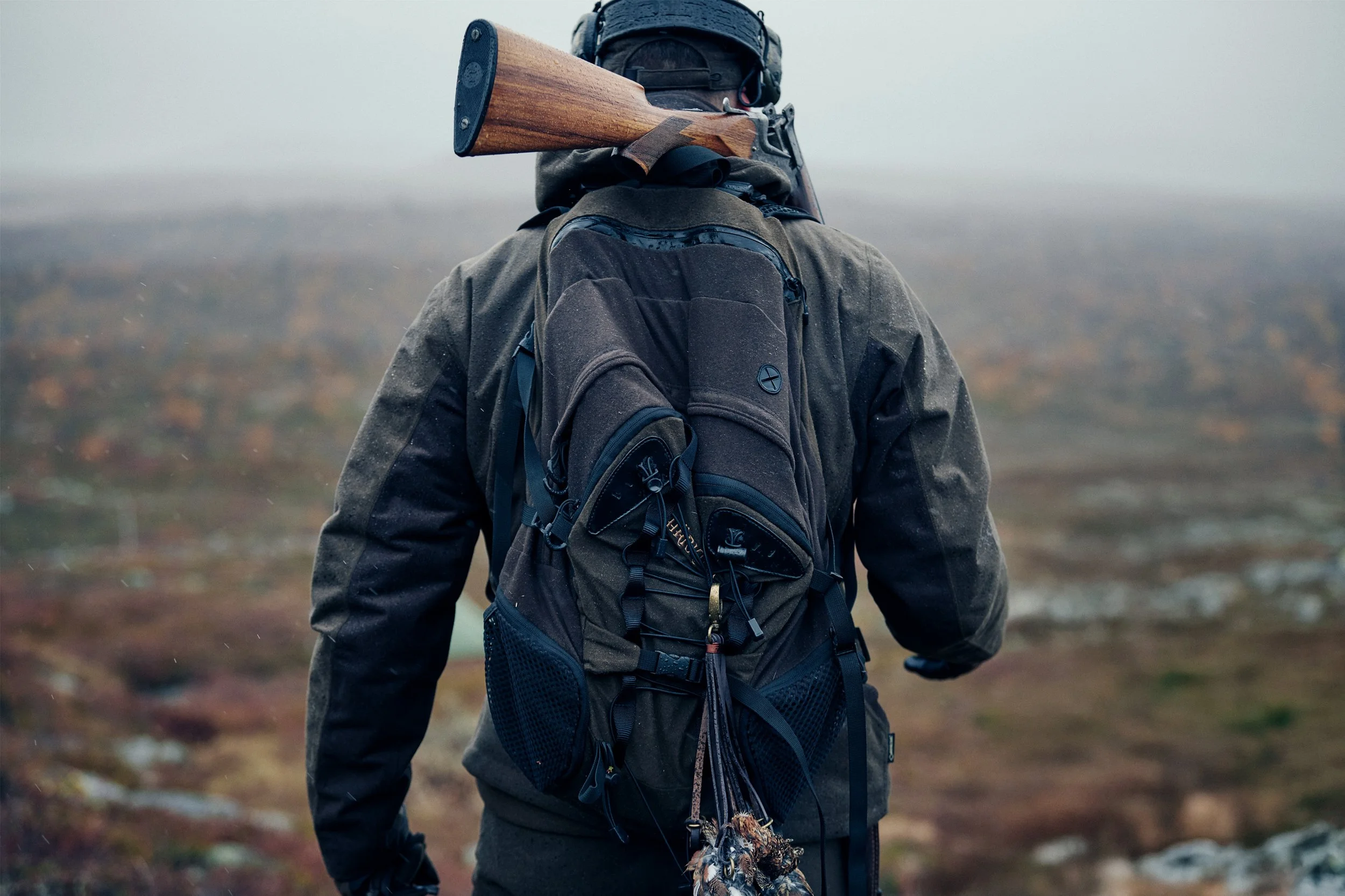 Hunter walking across open landscape carrying rifle and backpack, moving through terrain