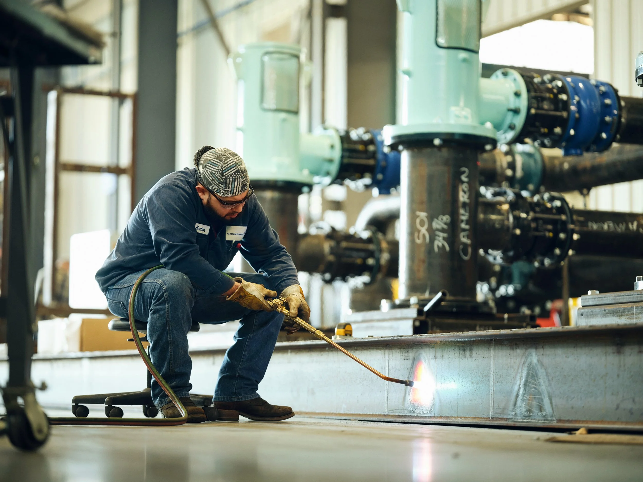 Technician using gas torch for metal work in industrial facility with large pipe systems