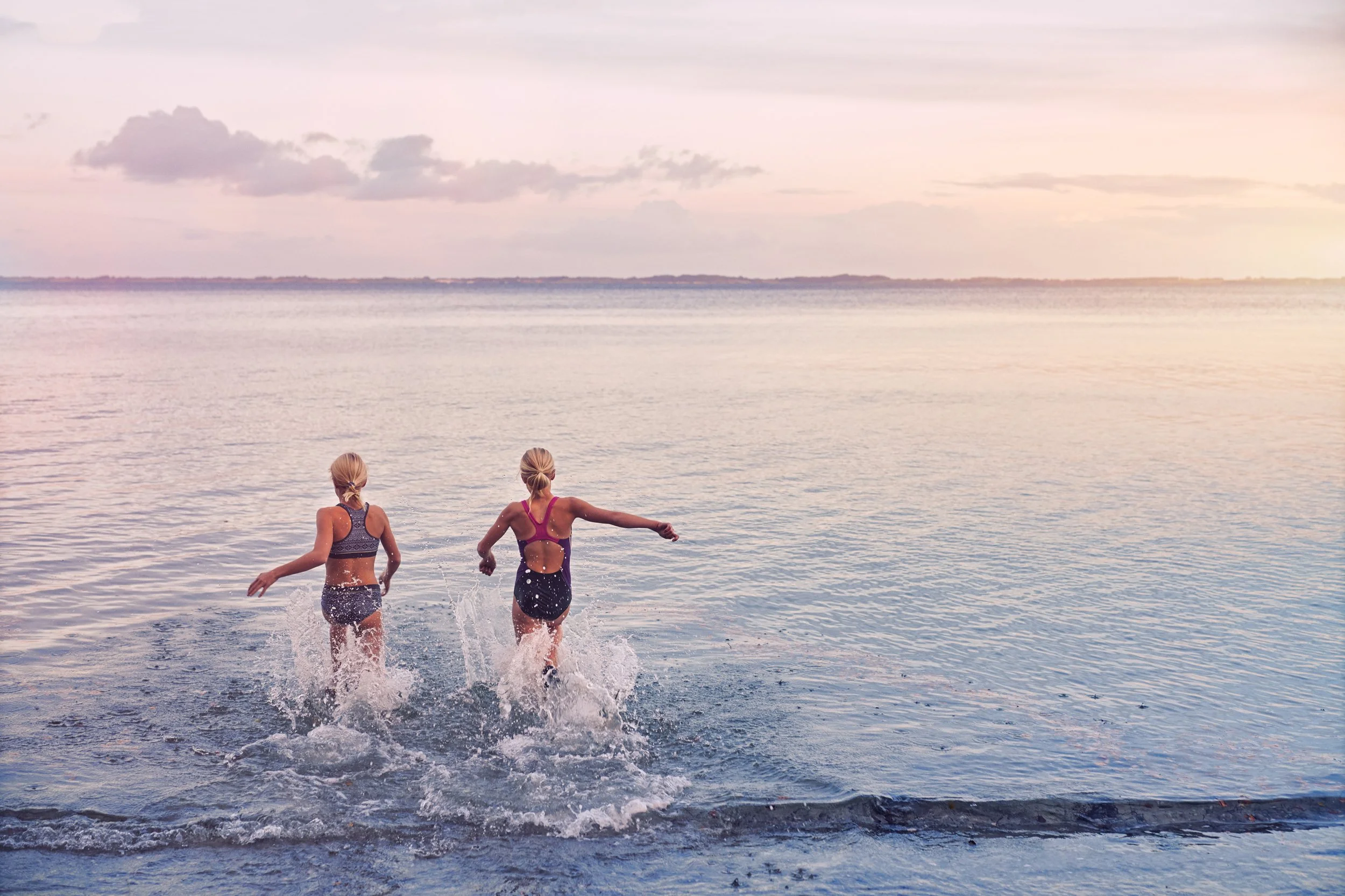 Two kids seen from the back running into water together, shared activity at shoreline