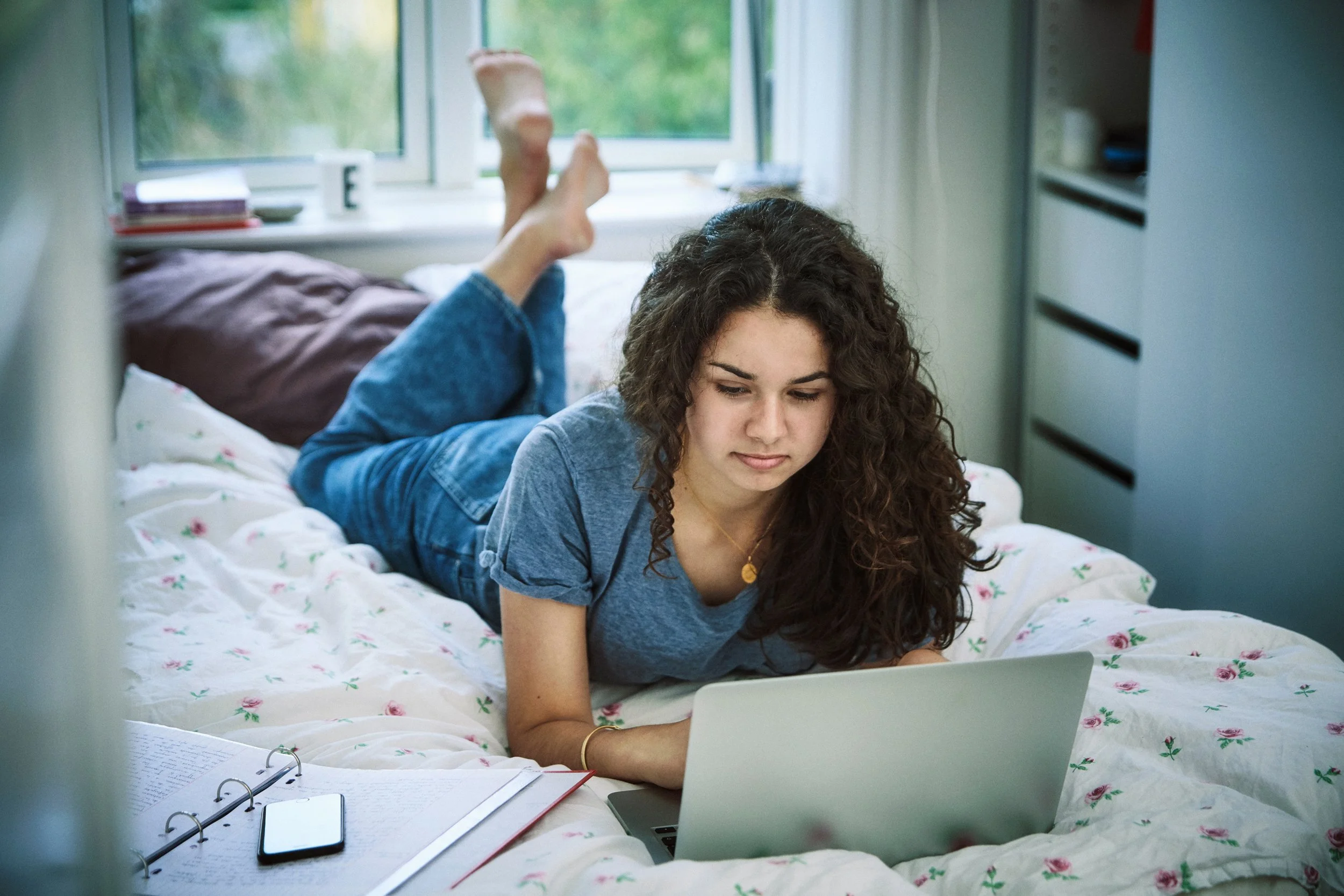 Young woman lying on bed using laptop, digital access in everyday setting
