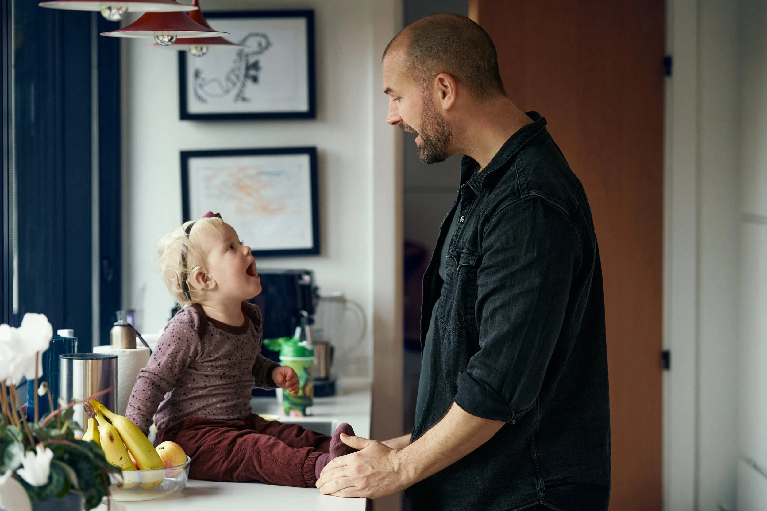Father speaking with child wearing hearing aids, engaged moment in kitchen