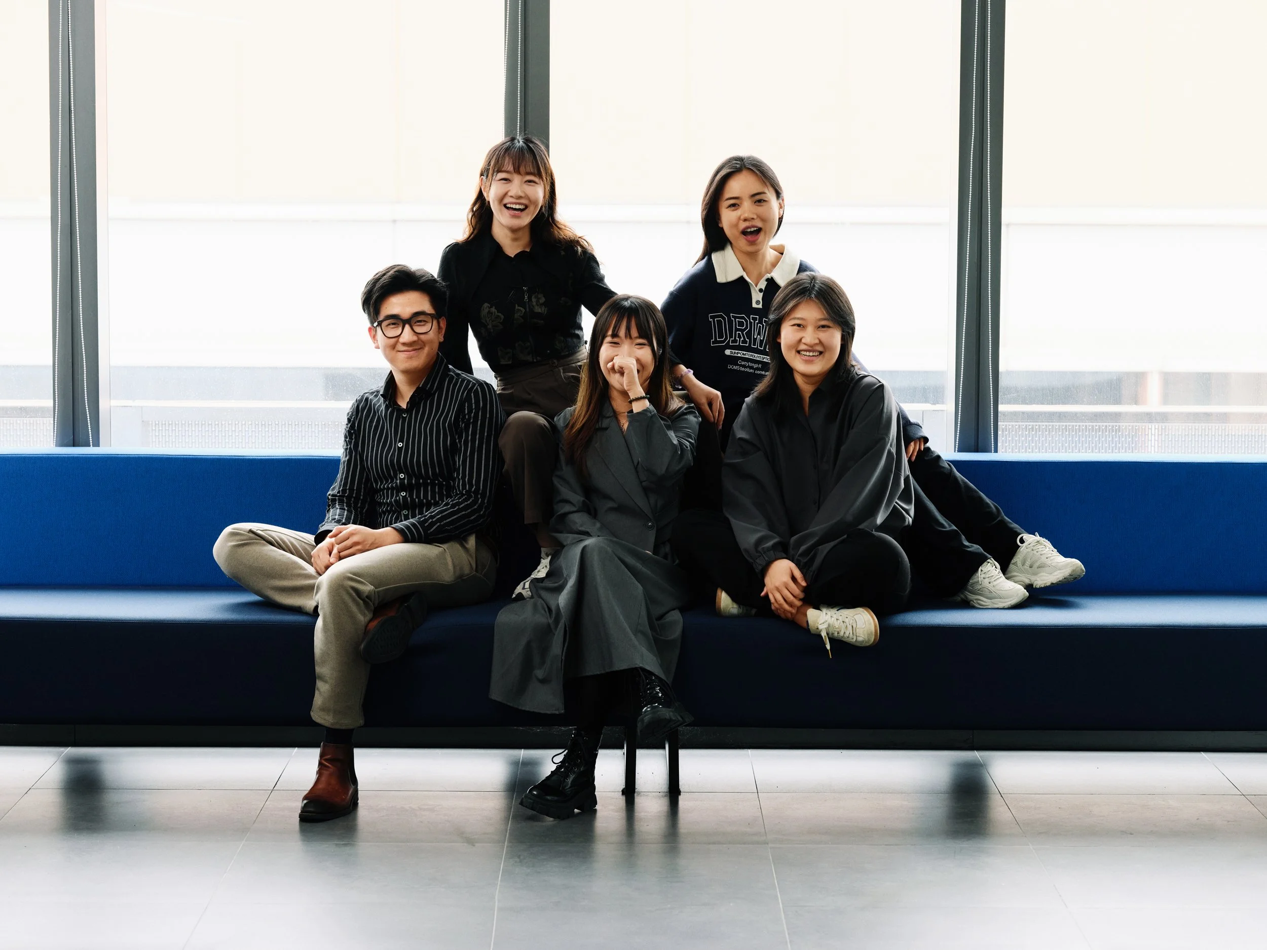 Group of young professionals sitting together on sofa in modern office, informal team portrait with natural interaction