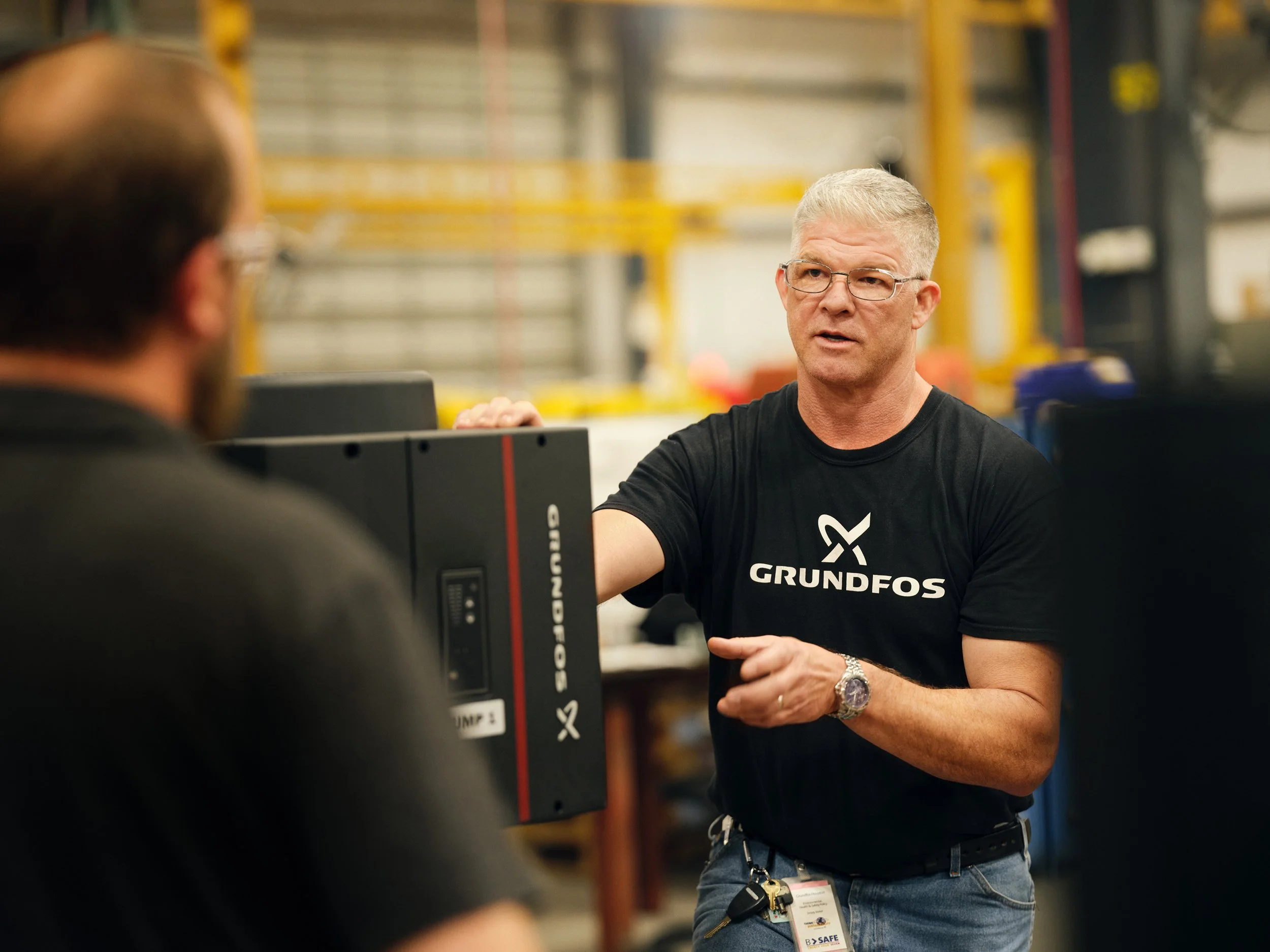 Engineer presenting equipment to colleague on factory floor, mid-conversation