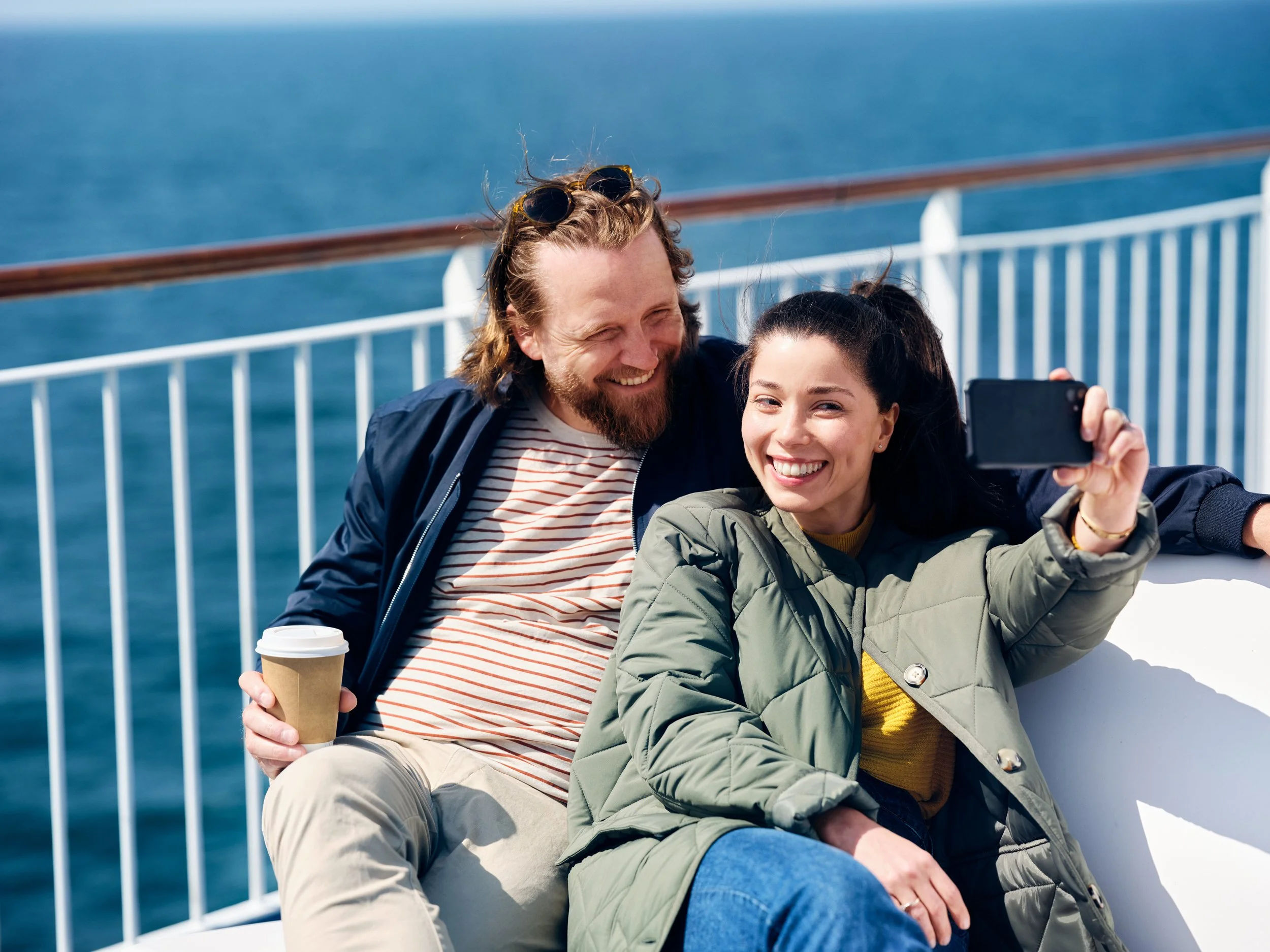 Couple taking selfie on ferry deck with ocean behind, shared travel experience