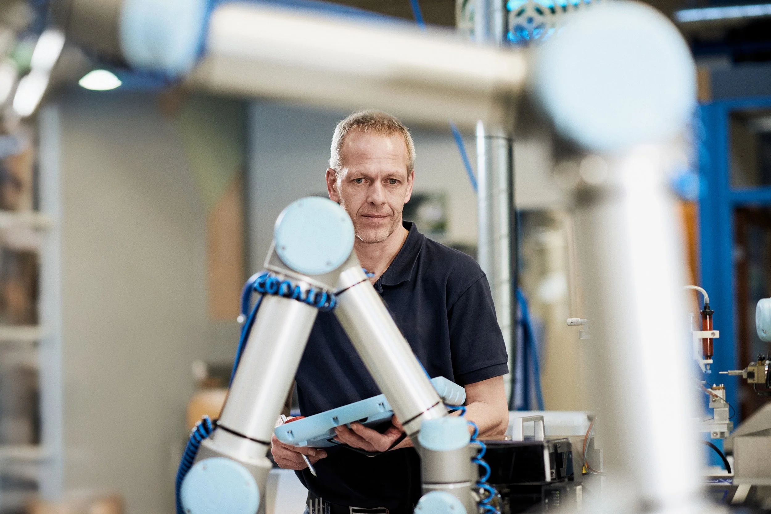 Technician controlling robotic arm in workshop environment focusing on precision task