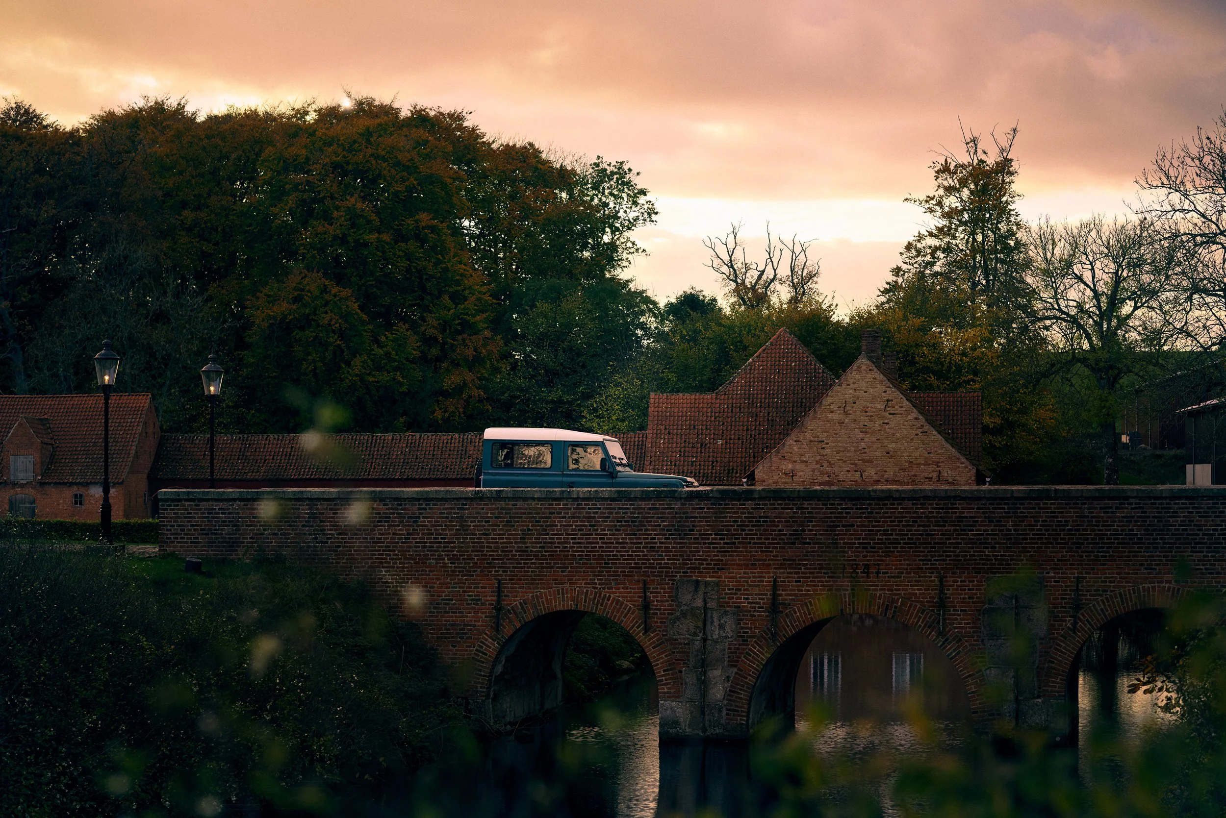 Off-road vehicle crossing bridge at sunset, rural landscape and evening atmosphere