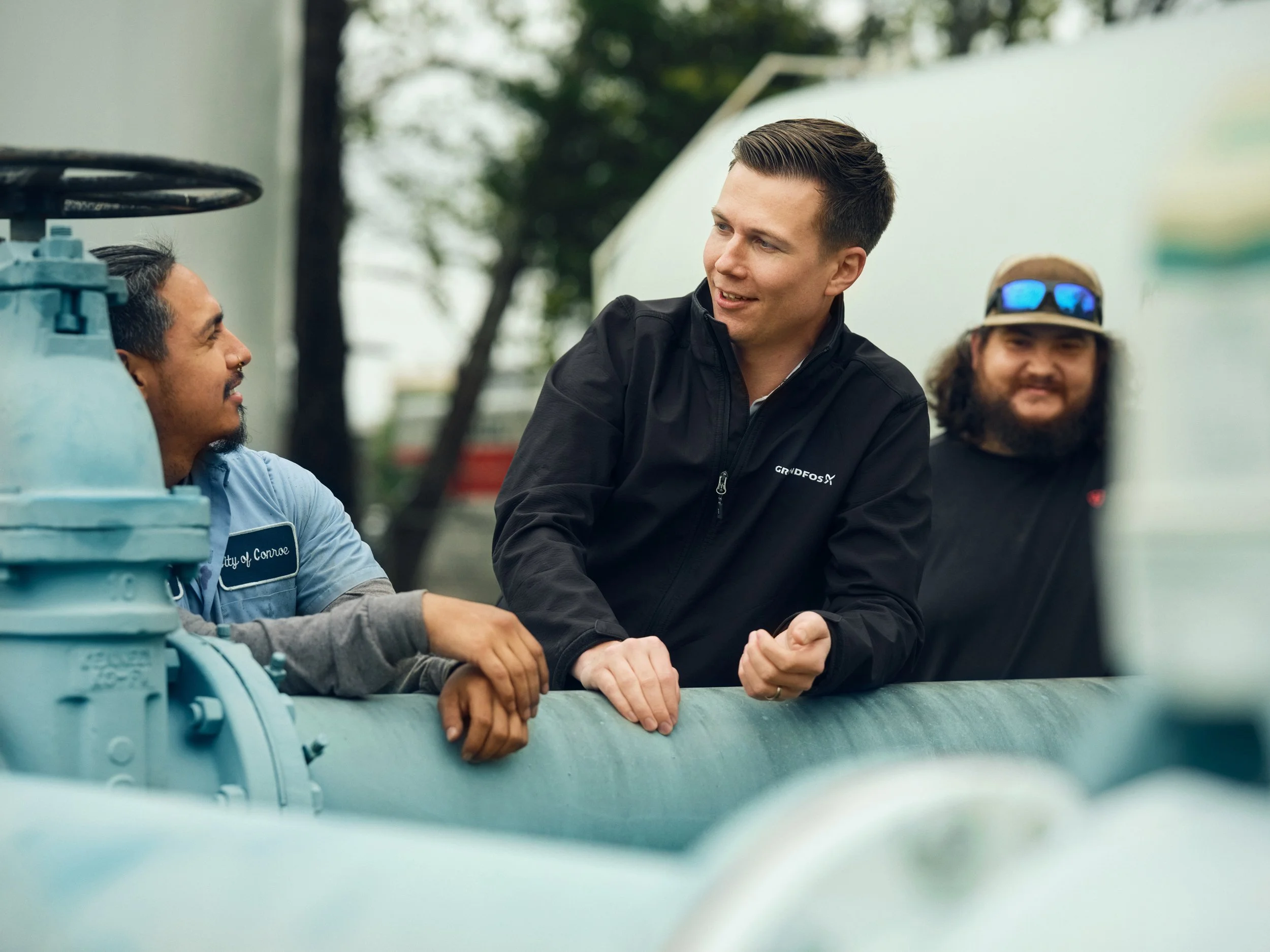 Three men talking around large blue pipe installation outdoors