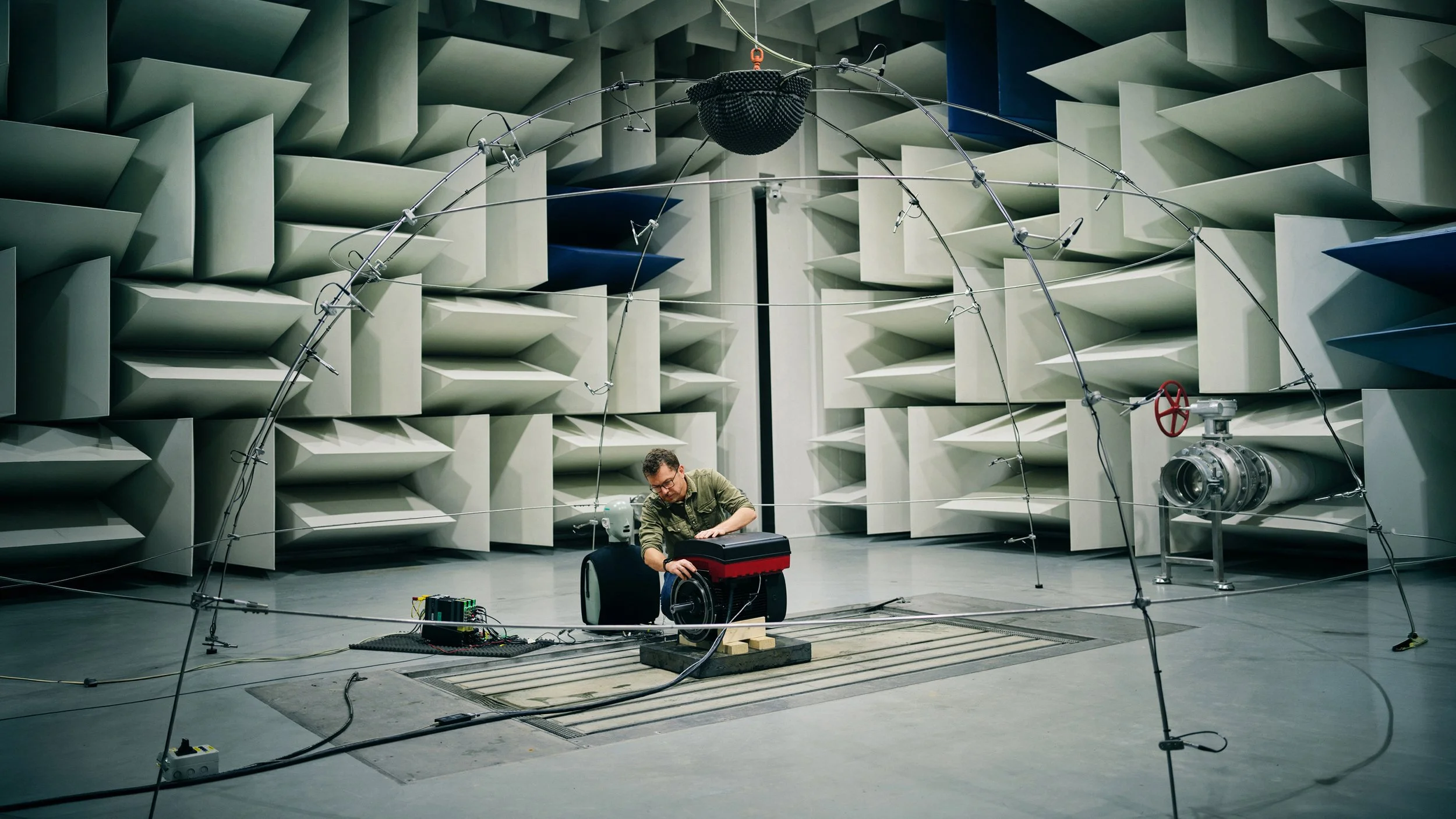 A man working with scientific equipment in an anechoic chamber with large foam wedges and metal rods.
