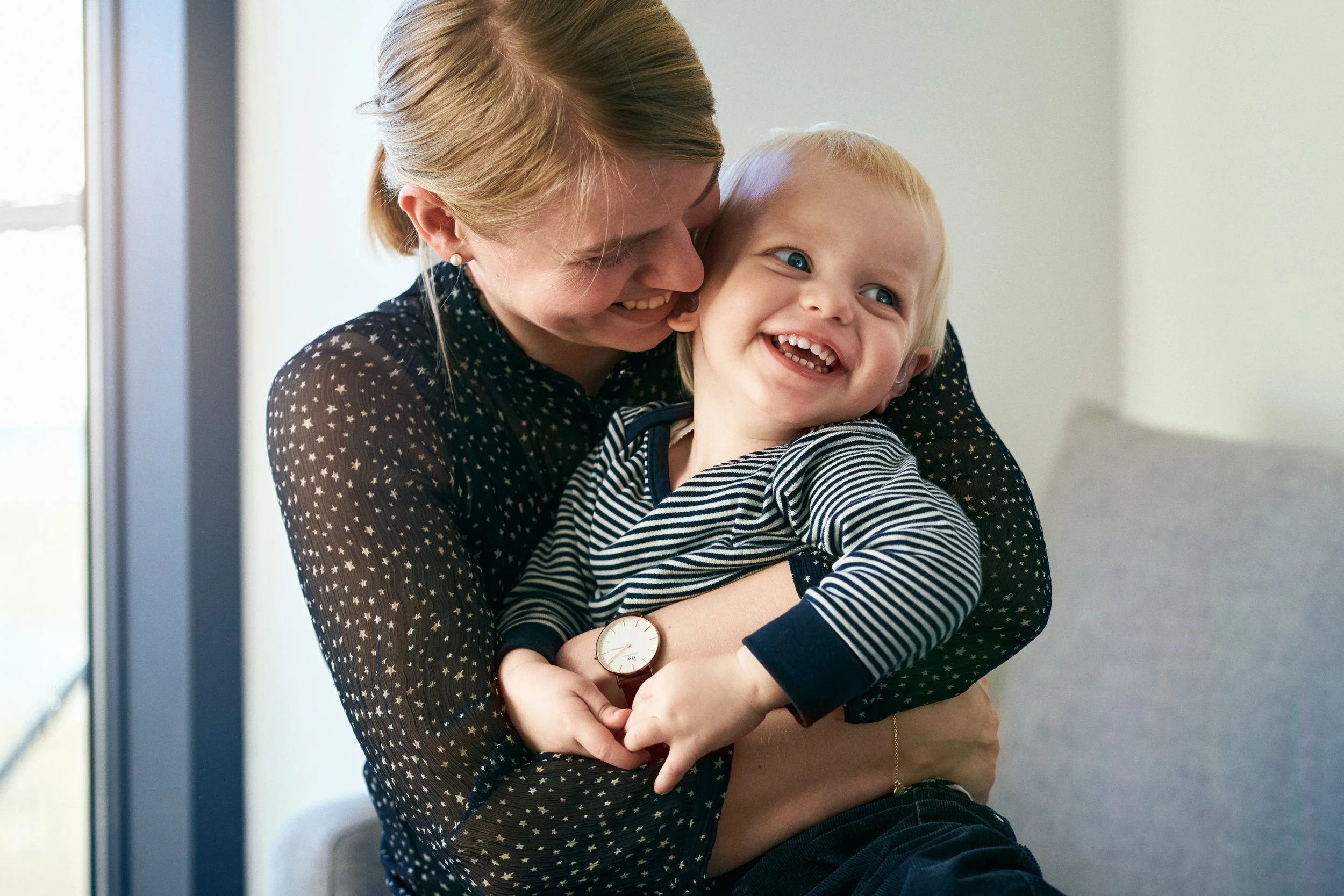 Mother holding child with cochlear implant, close and joyful interaction indoors