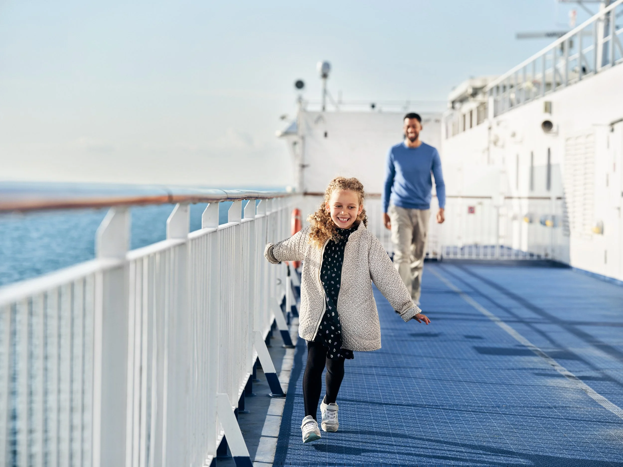 Child running along ferry deck with adult behind, movement and travel moment at sea