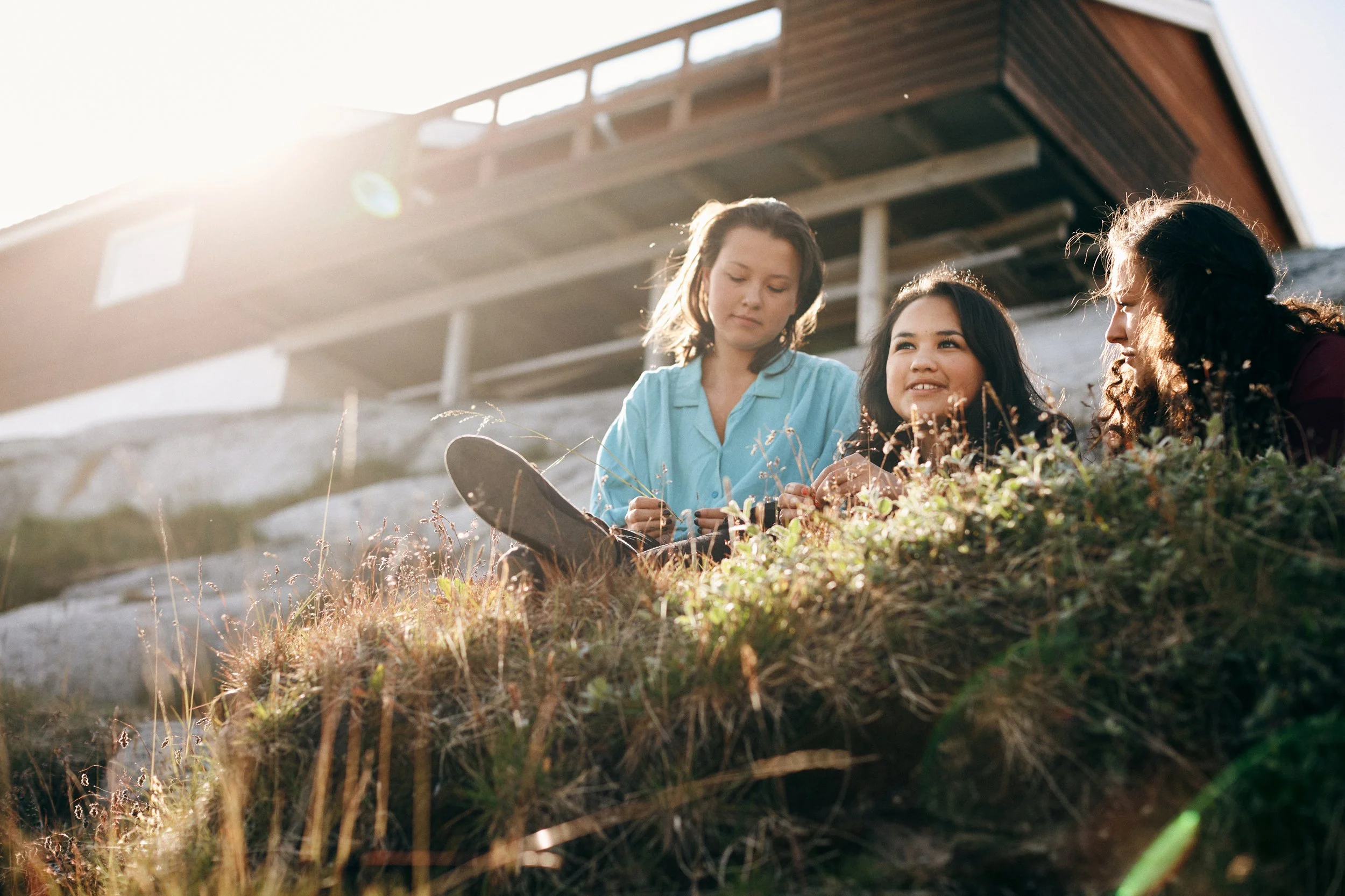 Three children sitting in grass outside house, calm moment in warm sunlight