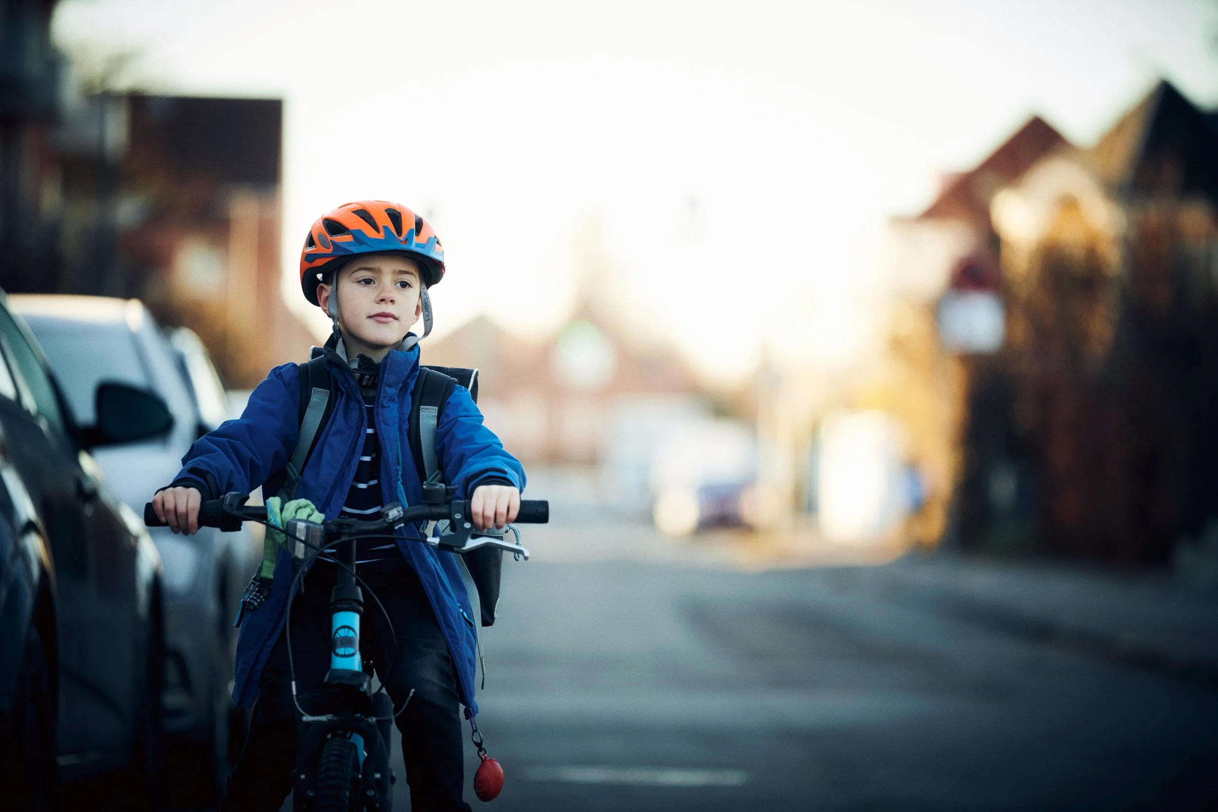 Child riding bicycle on residential street wearing helmet, everyday urban moment