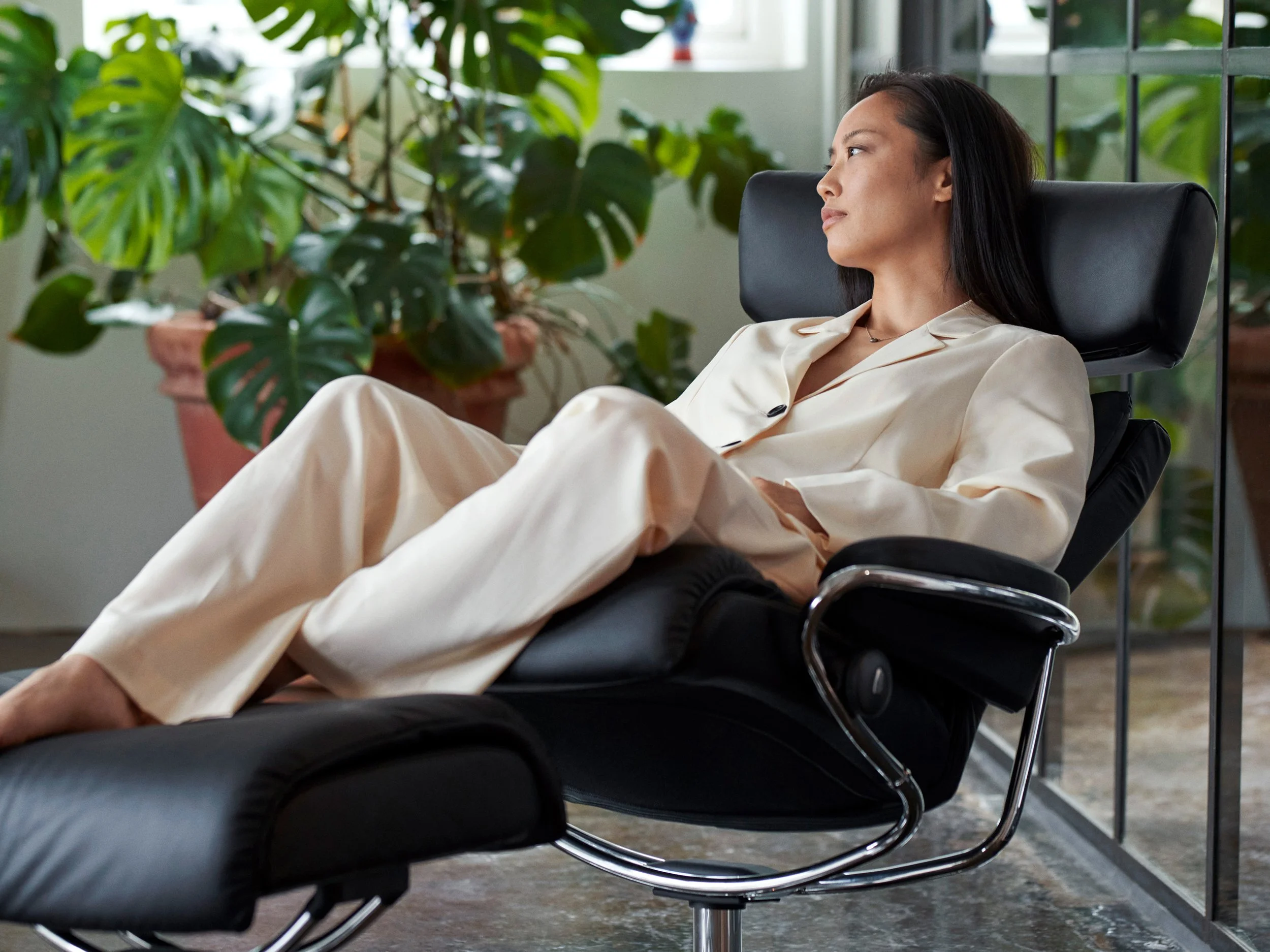 Woman reclining in chair surrounded by plants, relaxed indoor moment