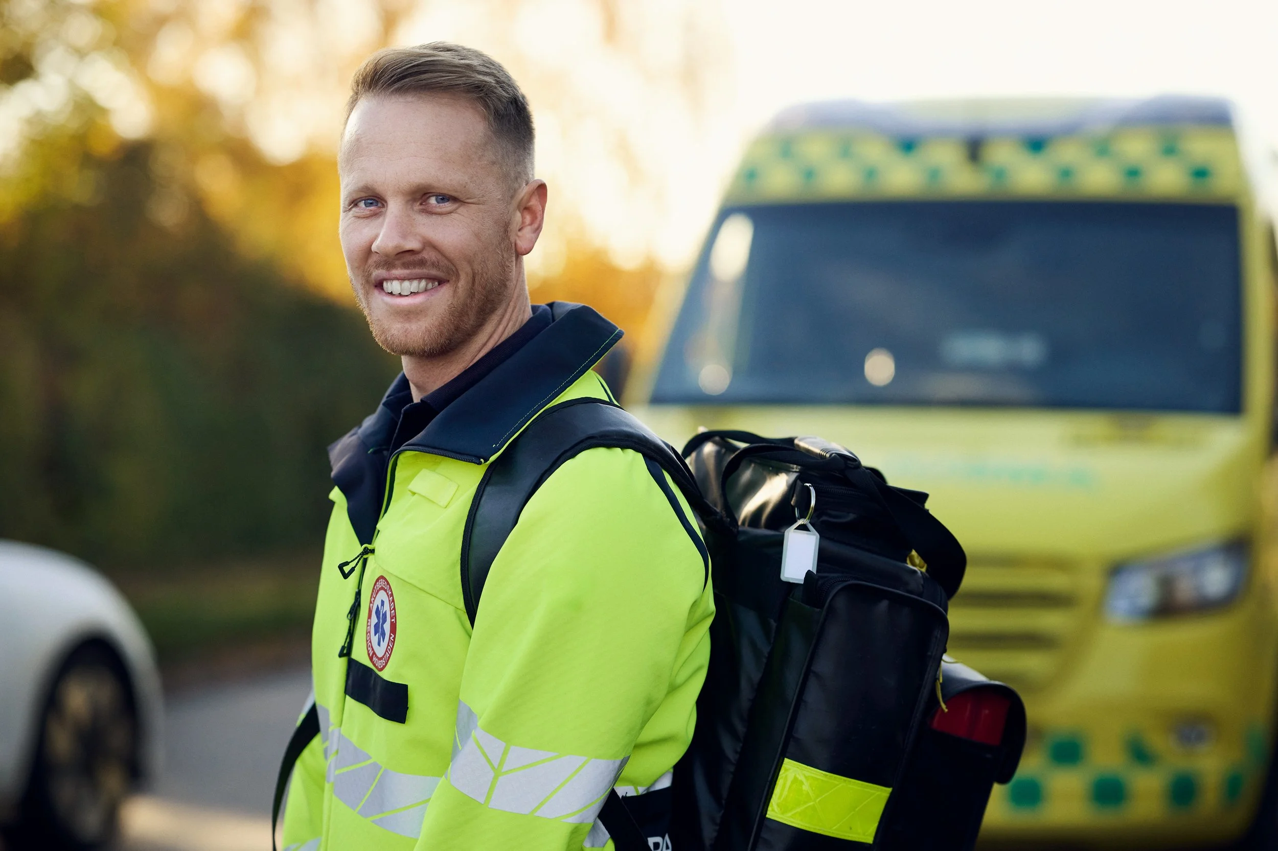 Paramedic standing outdoors in uniform with ambulance behind, portrait in work context
