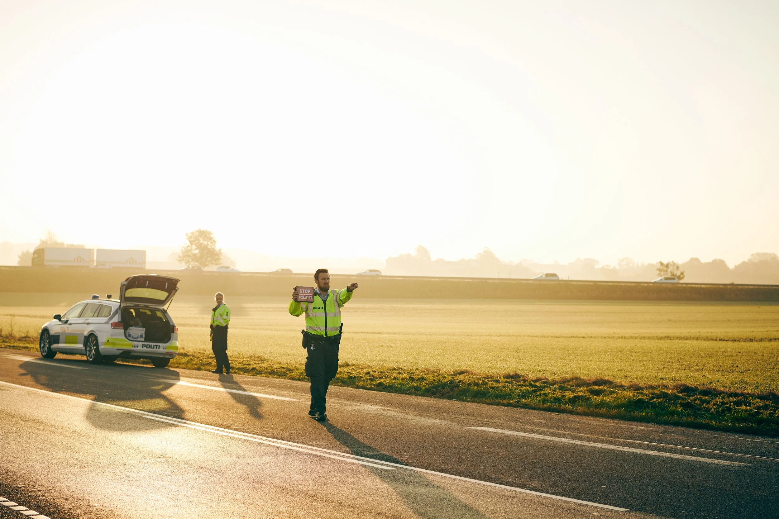 Police officer directing traffic on rural road with patrol car in background